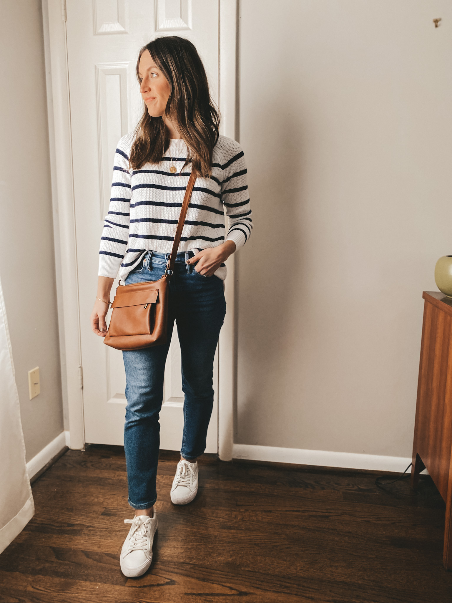 ashley wearing a white sweater with blue stripes from Old Navy, Madewell Perfect Vintage Jeans in a medium wash, Madewell white sneakers, and a cognac crossbody bag from Target