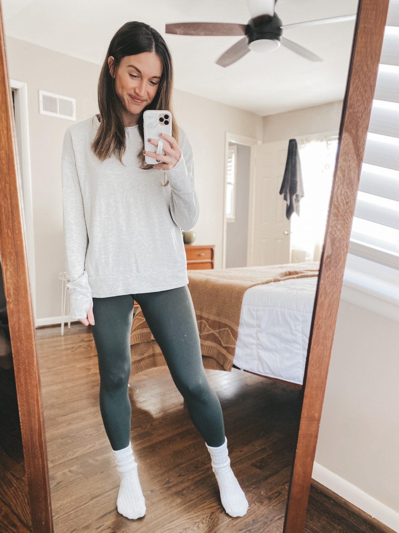ashley wearing a heather oatmeal colored sweatshirt from Aerie, olive green leggings from Aerie, and waffle socks from Target