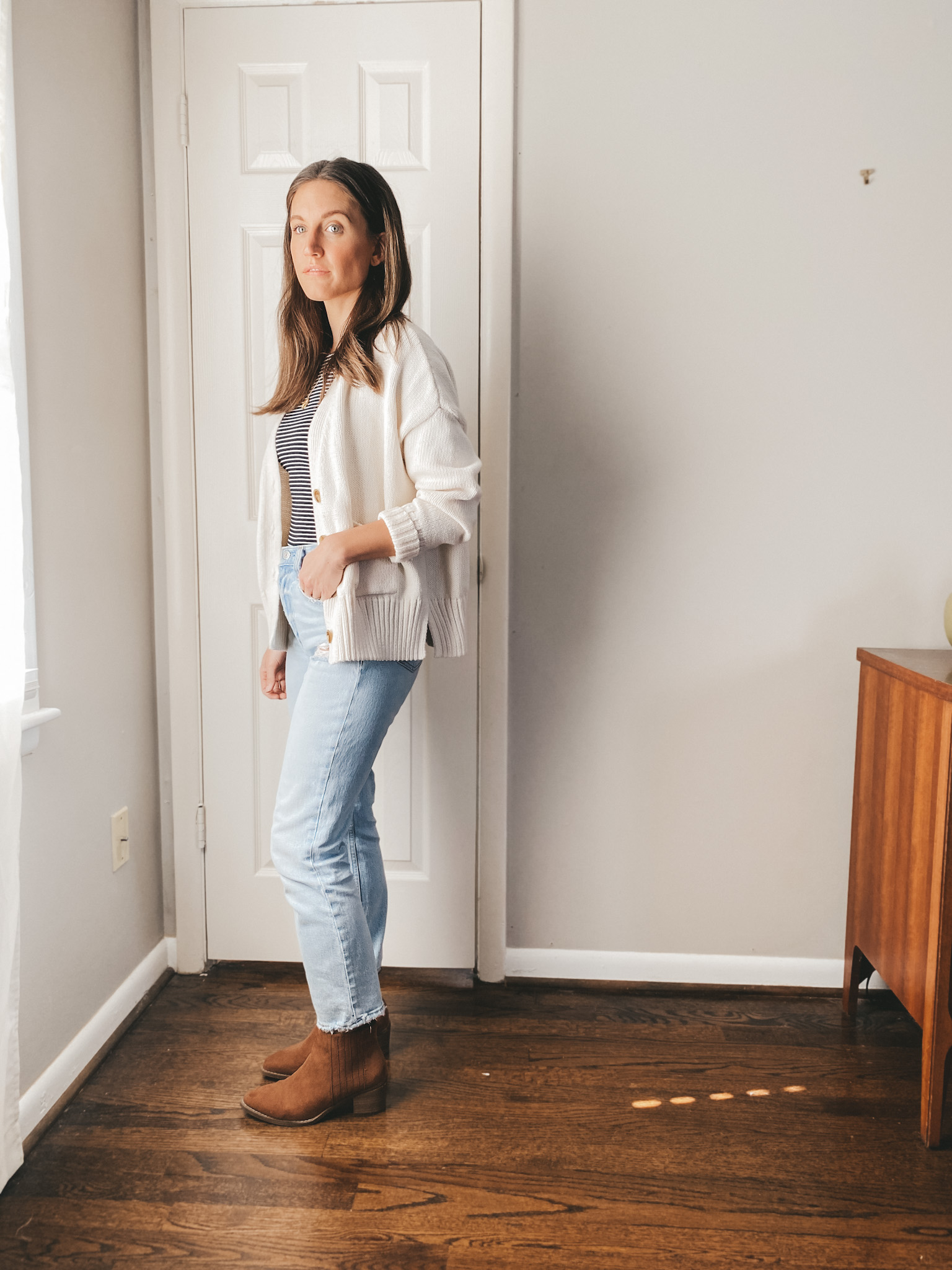 ashley wearing a striped bodysuit from Everlane under a cream button front cardigan from Target, mom jeans from Abercrombie and cognac booties from Target