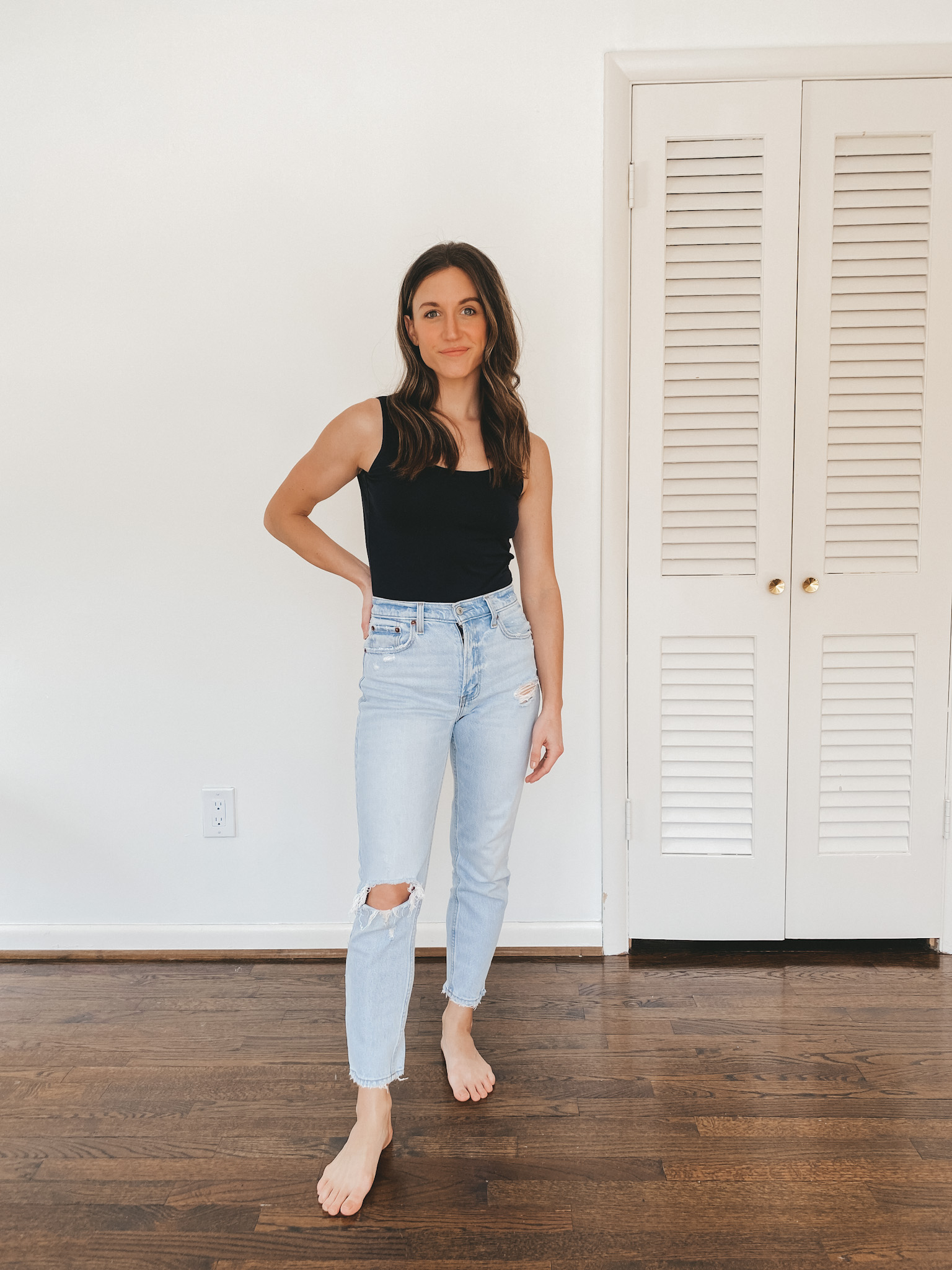 Ashley wearing a black sleeveless bodysuit from Everlane and light wash distressed mom jeans from Abercrombie
