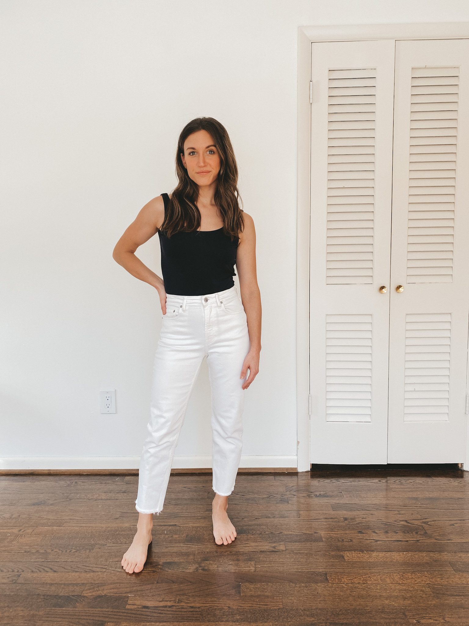 Ashley wearing a black Everlane sleeveless bodysuit and white Everlane straight leg jeans.