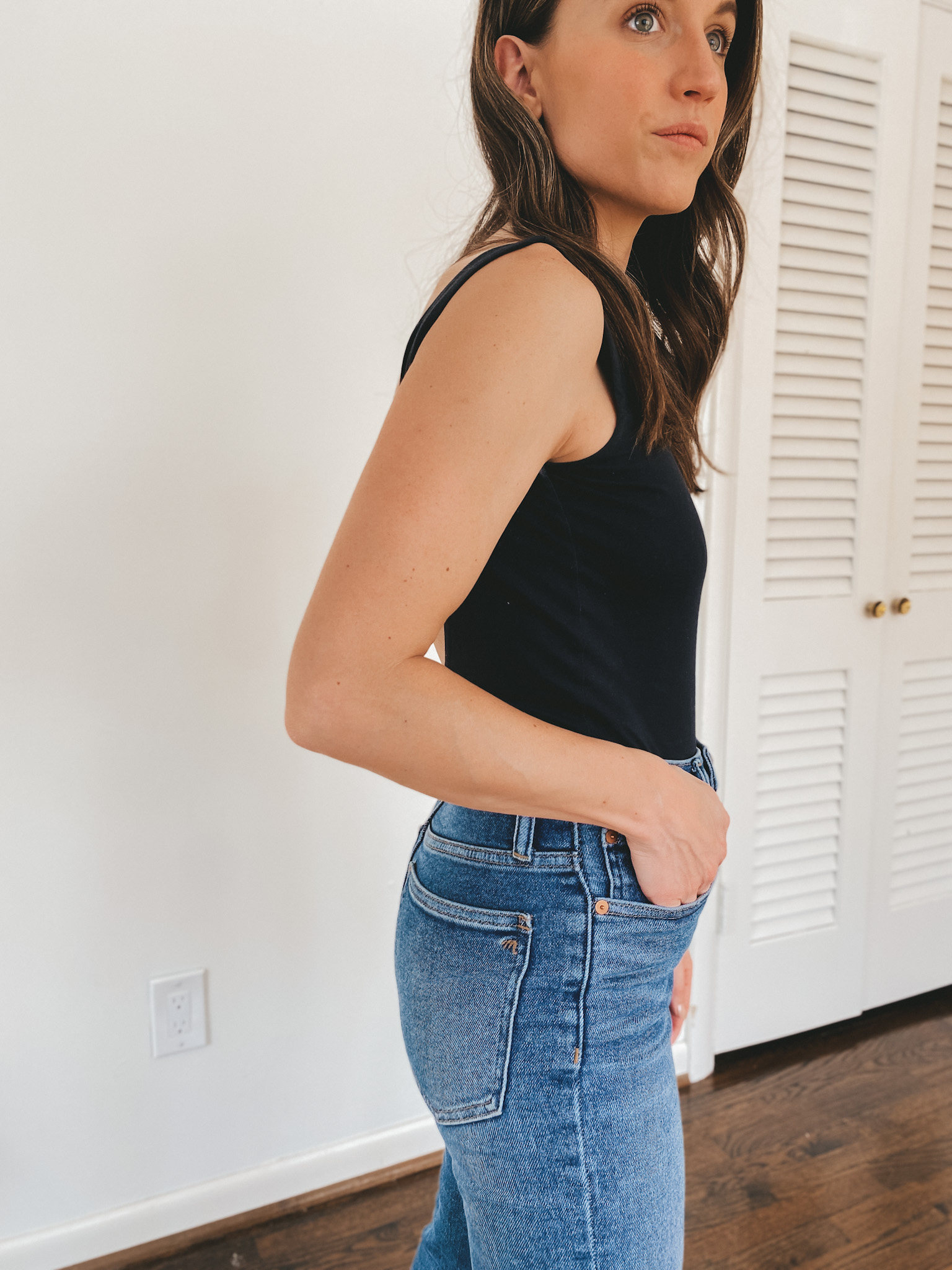 ashley wearing a black sleeveless bodysuit from Everlane and Perfect Vintage Jeans from Madewell