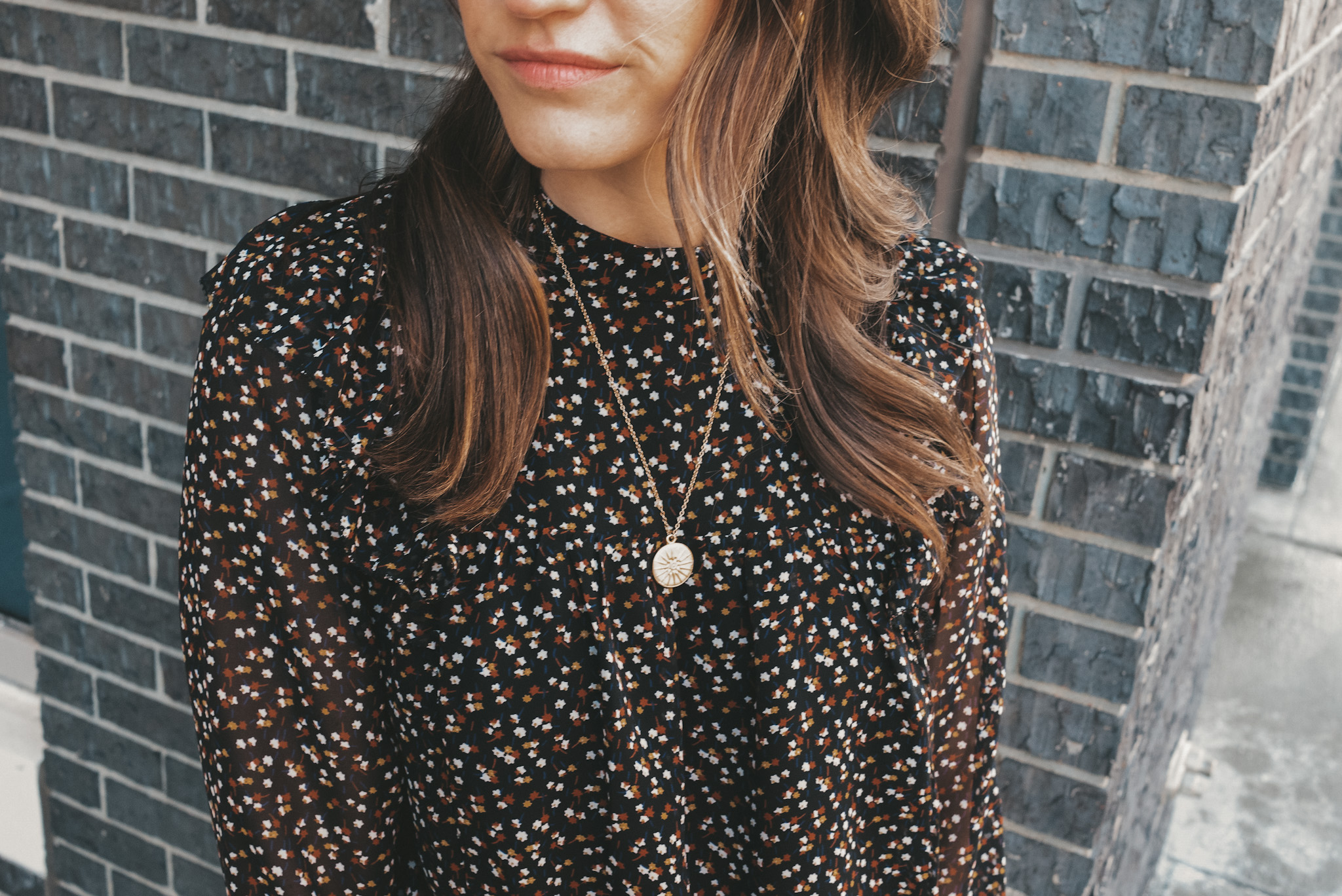 ashley wearing simple jewelry including gold hoop earrings, a pendant necklace and gold bangle with a black floral top