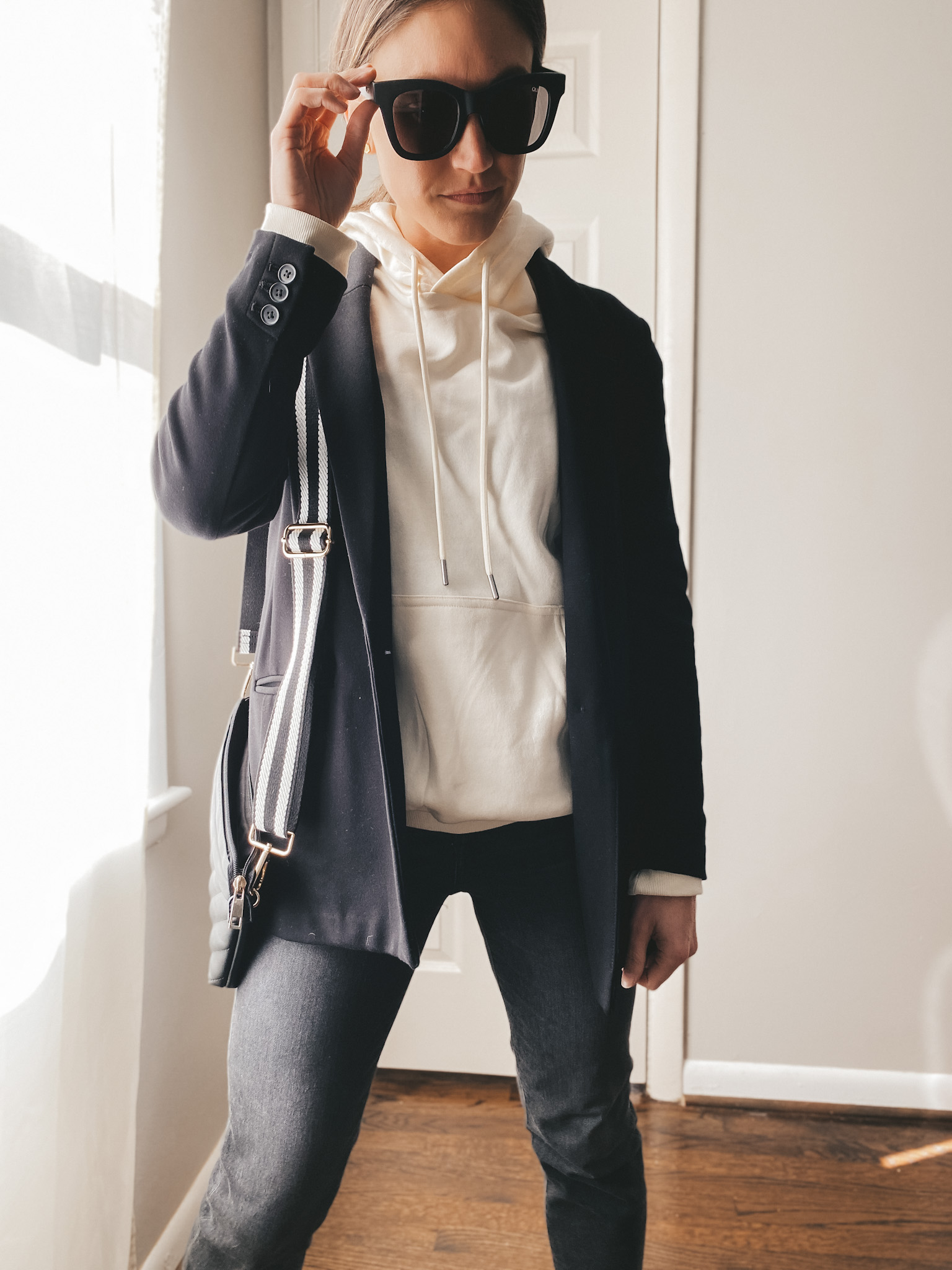 ashley wearing a cream hoodie from H&M, black blazer from Old Navy, Sunglasses from Quay, Jeans from Madewell