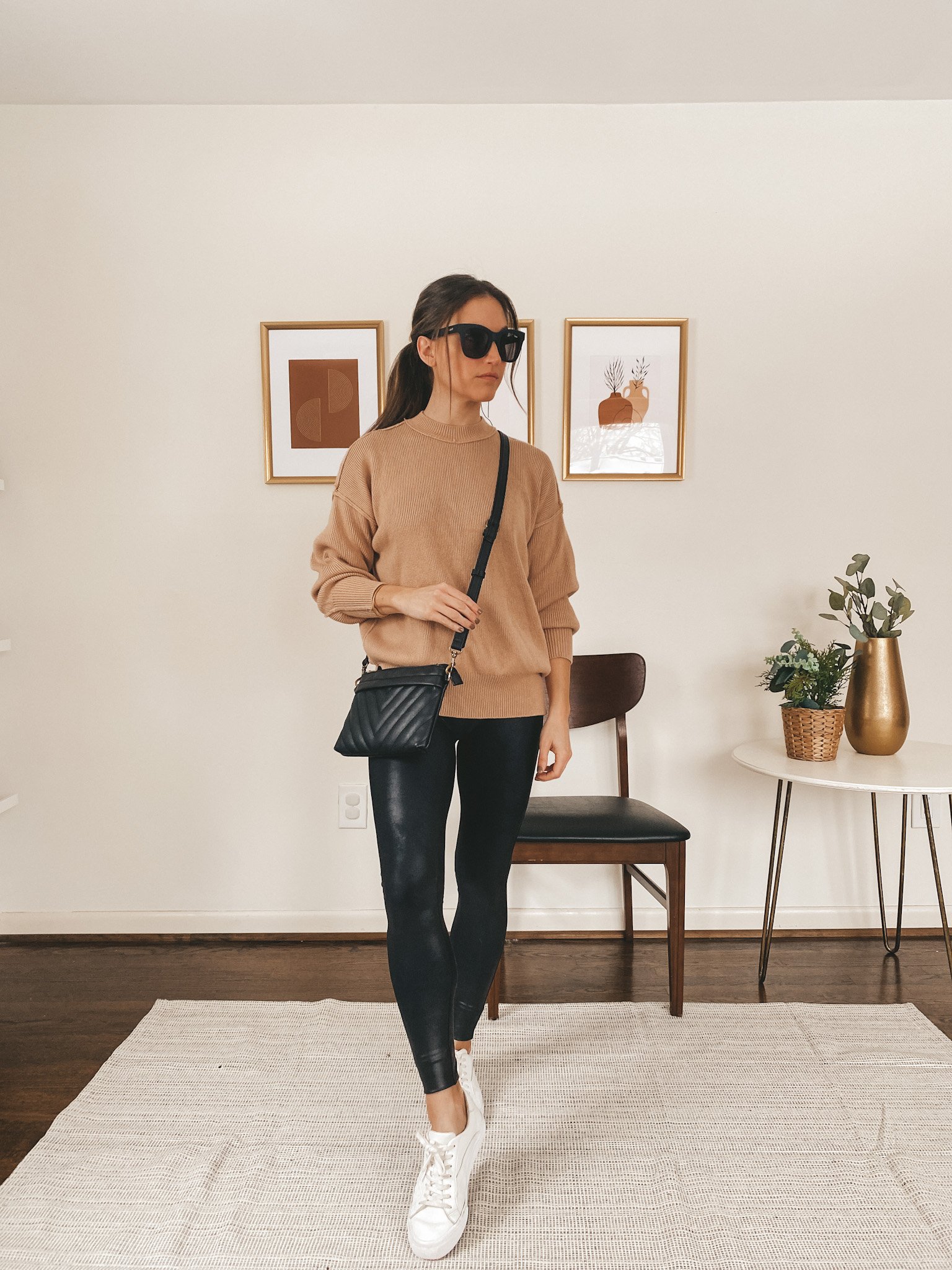 ashley wearing a tan oversized ribbed sweater from Abercrombie, Spanx faux leather leggings, black sunglasses from Quay Australia, white sneakers from Madewell and a quilted crossbody purse