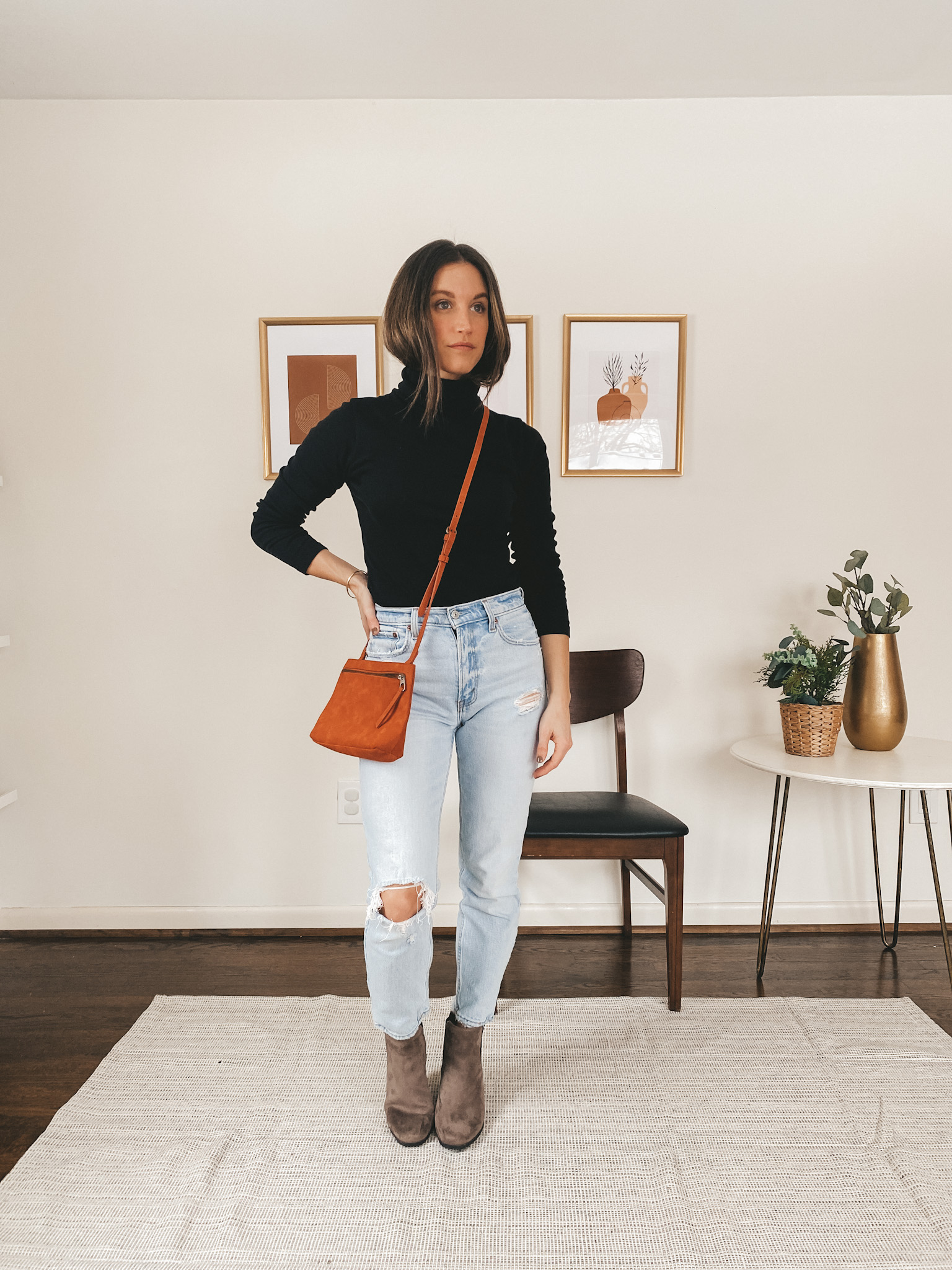 ashley wearing a black turtleneck from J.Crew, light wash distressed mom jeans from Abercrombie, brown Chelsea boots from Target, and a red crossbody bag from Target
