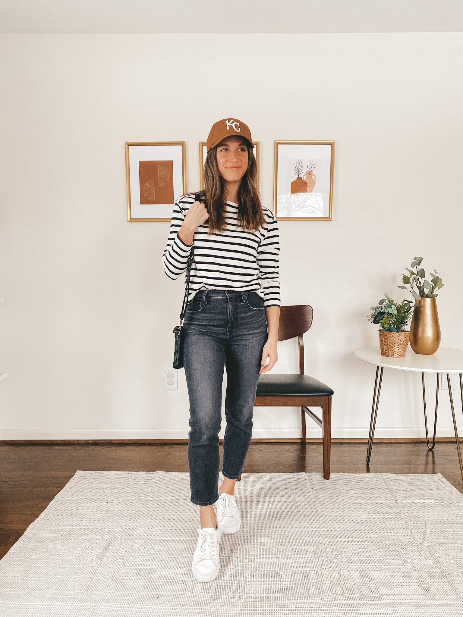 ashley wearing a black and white striped top from Everlane, washed black vintage jeans from Madewell, white sneakers from Madewell, a black quilted crossbody bag, and a brown KC baseball hat