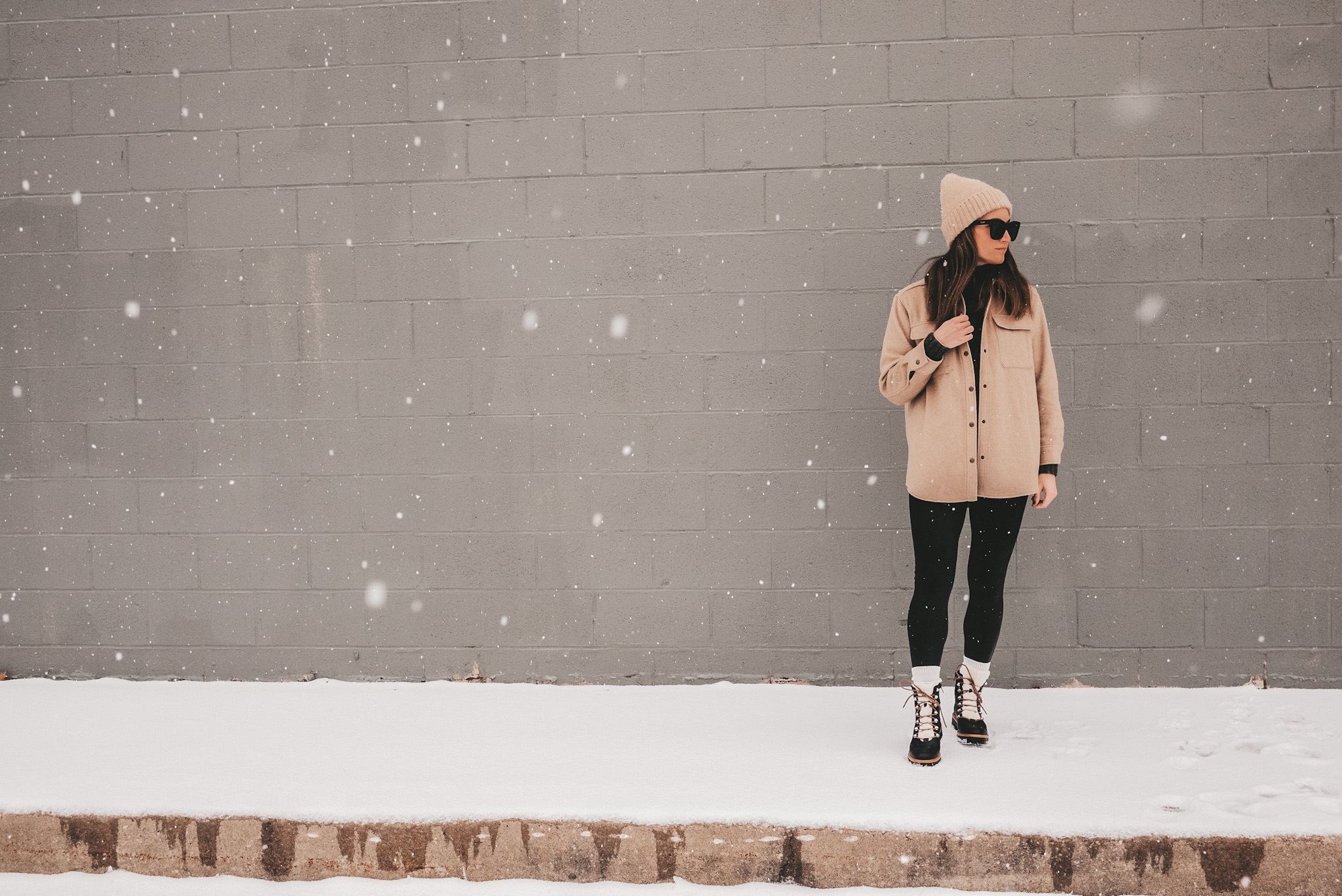 ashley standing on a snowy sidewalk with a gray brick background