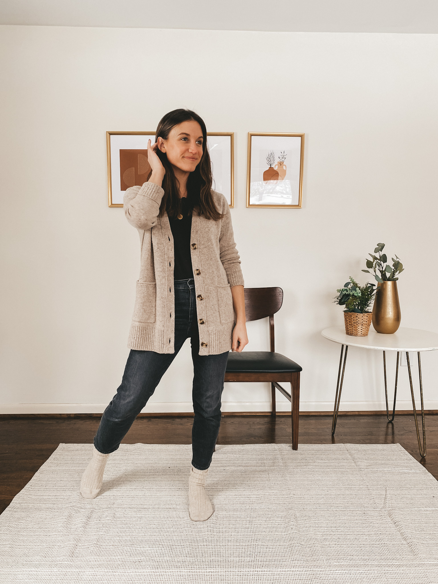 ashley wearing a black tee with a taupe button down cardigan, washed black straight leg jeans and taupe socks