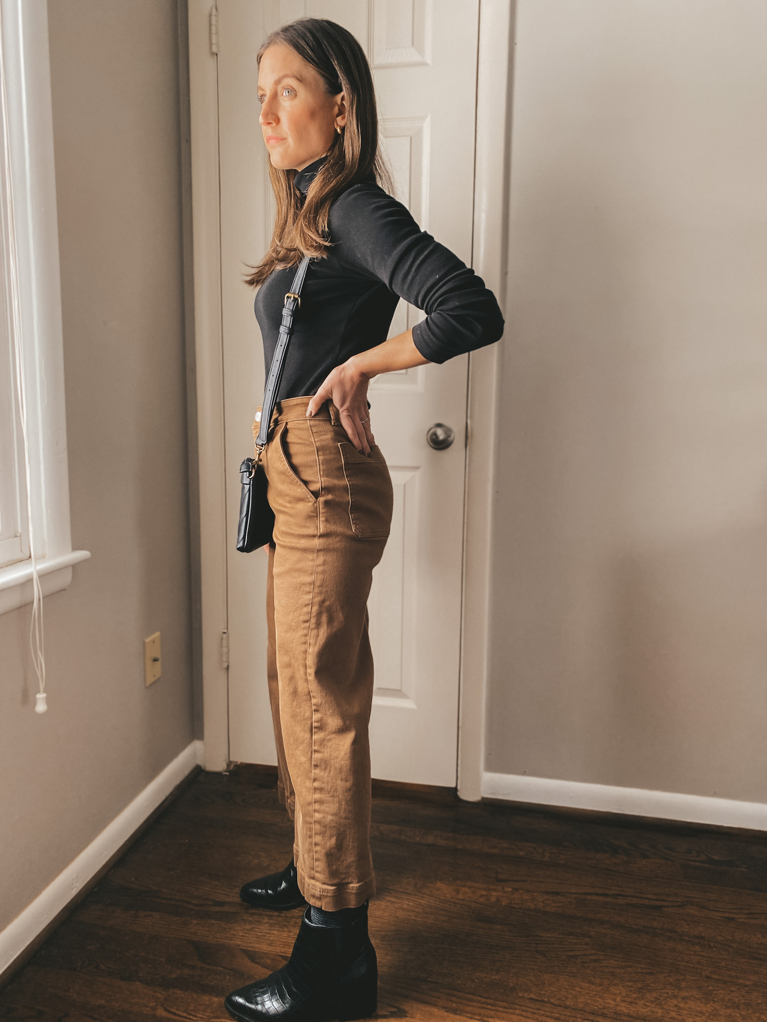 ashley wearing a fitted black turtleneck, ochre wide leg pants, and black boots