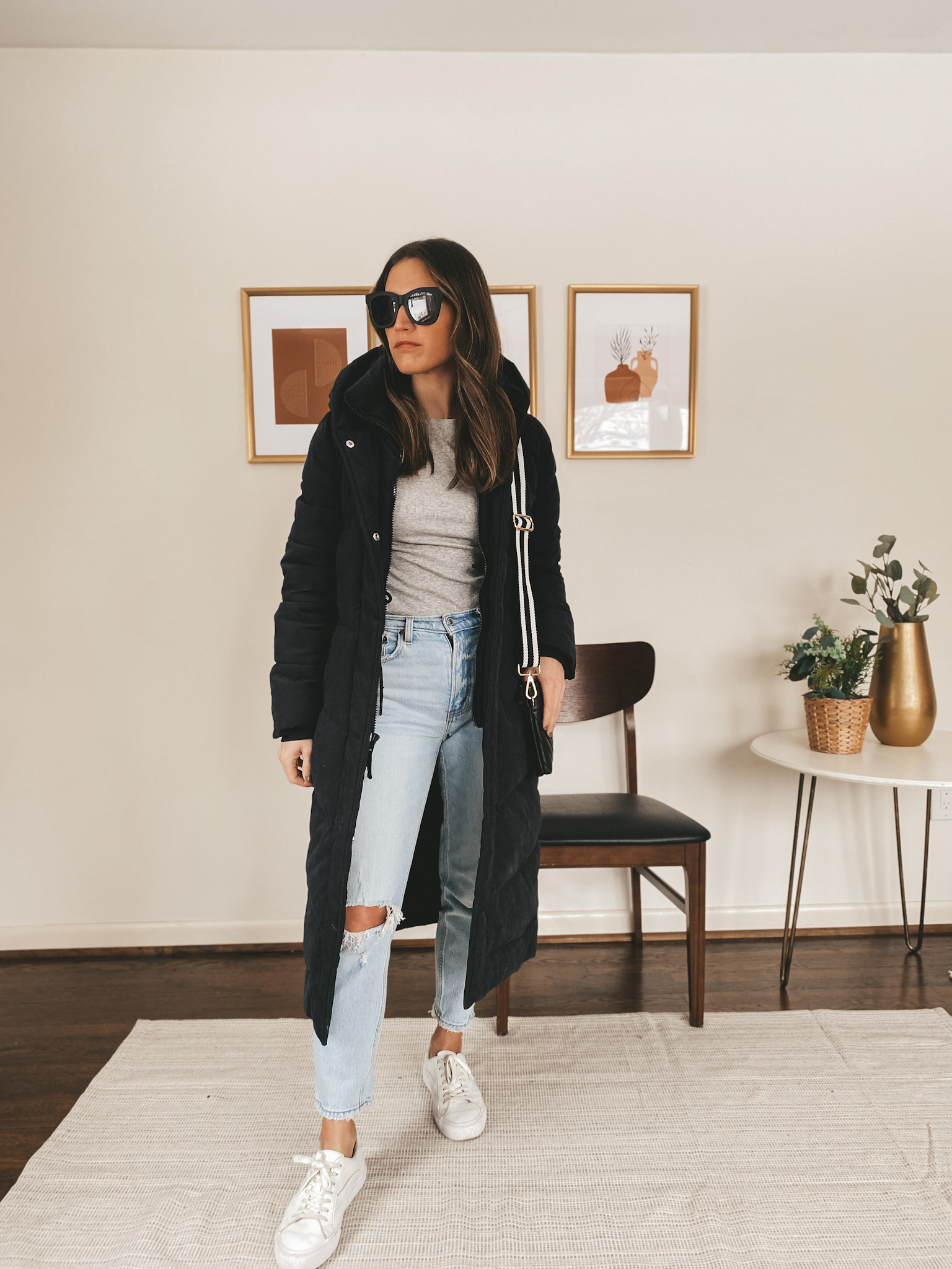 ashley wearing a gray tee from Target, a black long line puffer from Abercrombie, light wash distressed jeans, white sneakers from Madewell, and black sunglasses from Quay Australia