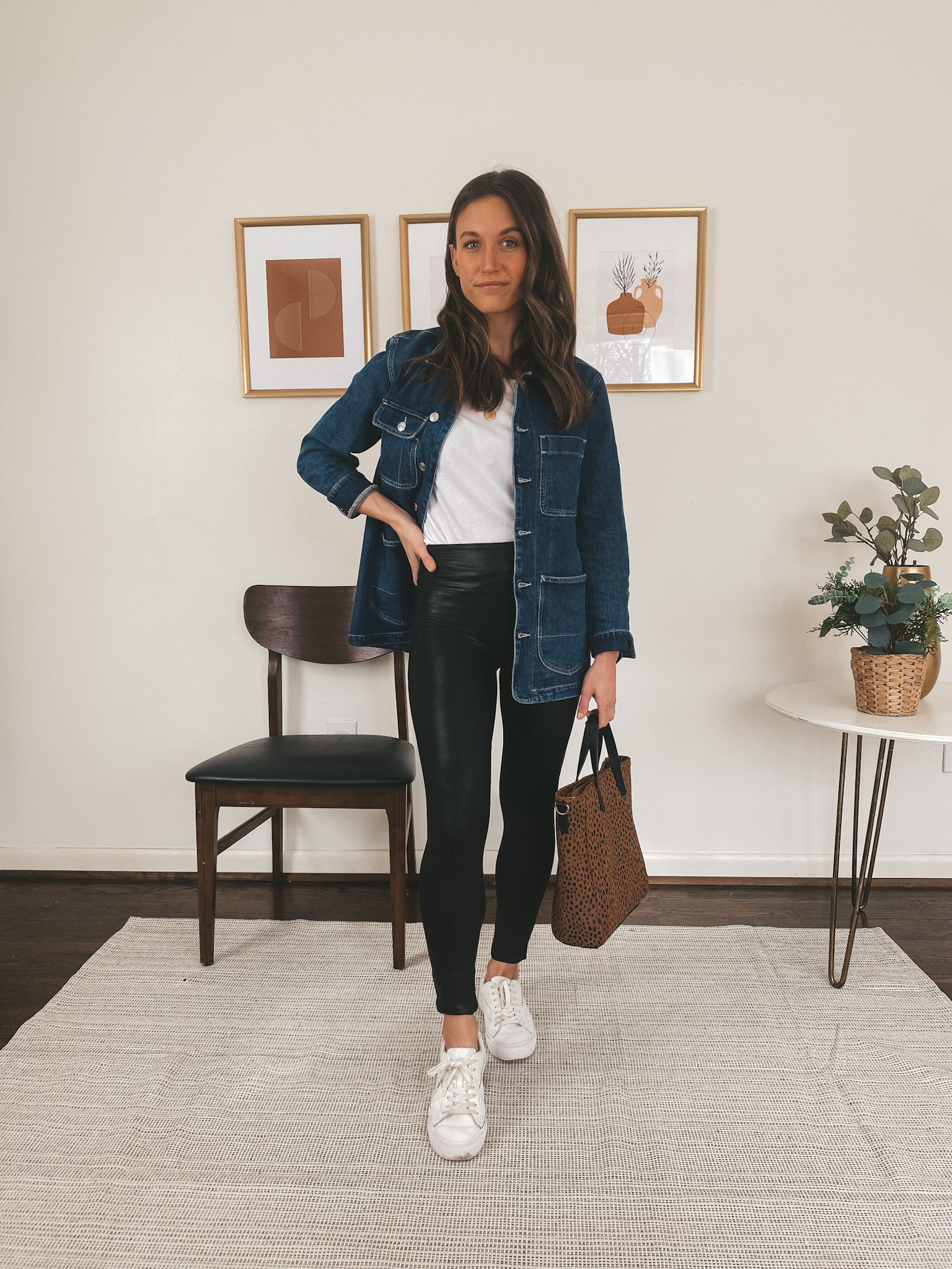 ashley wearing an Everlane white tee, a denim jacket, Spanx faux leather leggings, white Madewell sneakers, holding a leopard tote bag