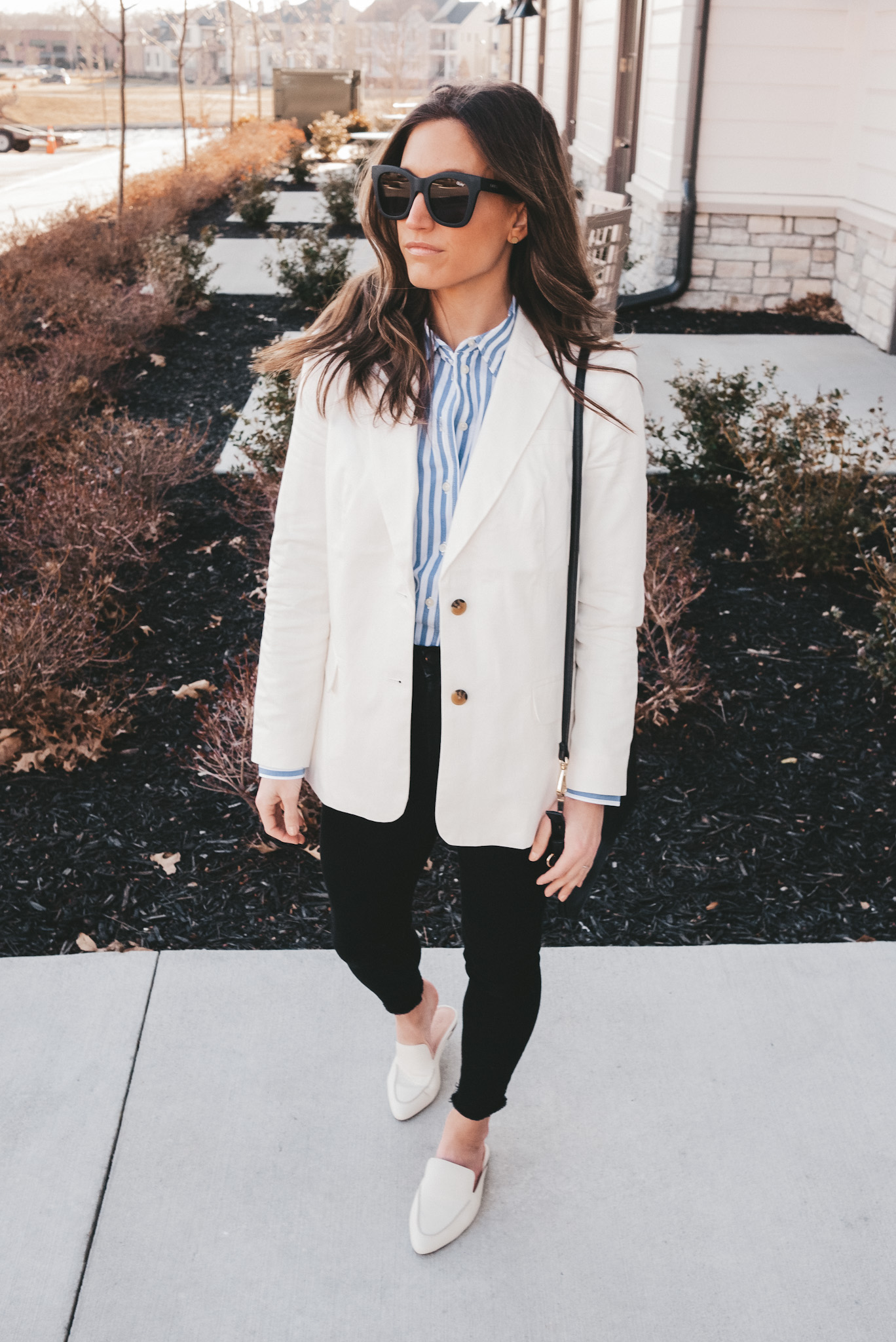 ashley wearing a Walmart white blazer, a Walmart blue and white striped button down, Everlane skinny jeans, and Madewell white loafers, standing on a sidewalk in front of a white building