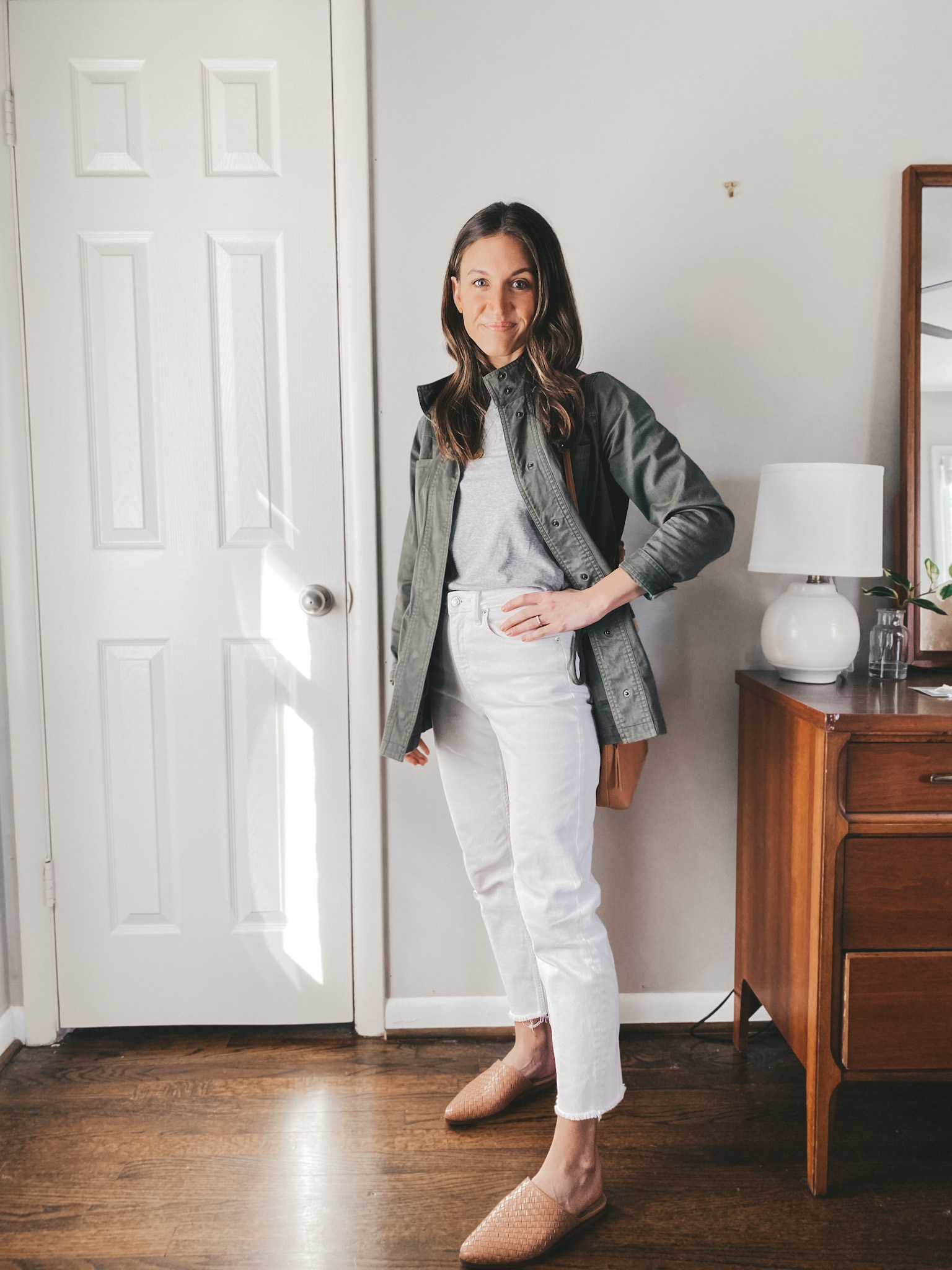 ashley wearing a Target green utility jacket, an Everlane gray tee, white Everlane straight leg jeans, and Marc Fischer tan woven mules