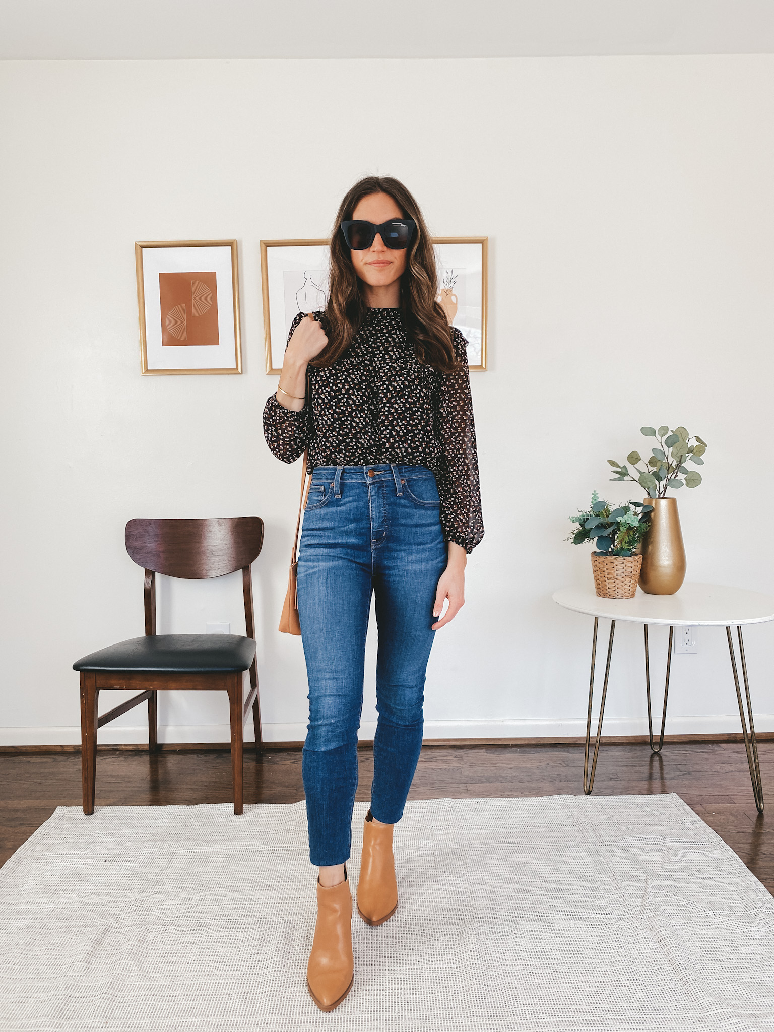 ashley wearing a Madewell puff sleeve blouse in black with a small flower pattern, Madewell skinny jeans, Target ankle booties in camel, a camel colored Target crossbody bag, and black square frame Quay sunglasses