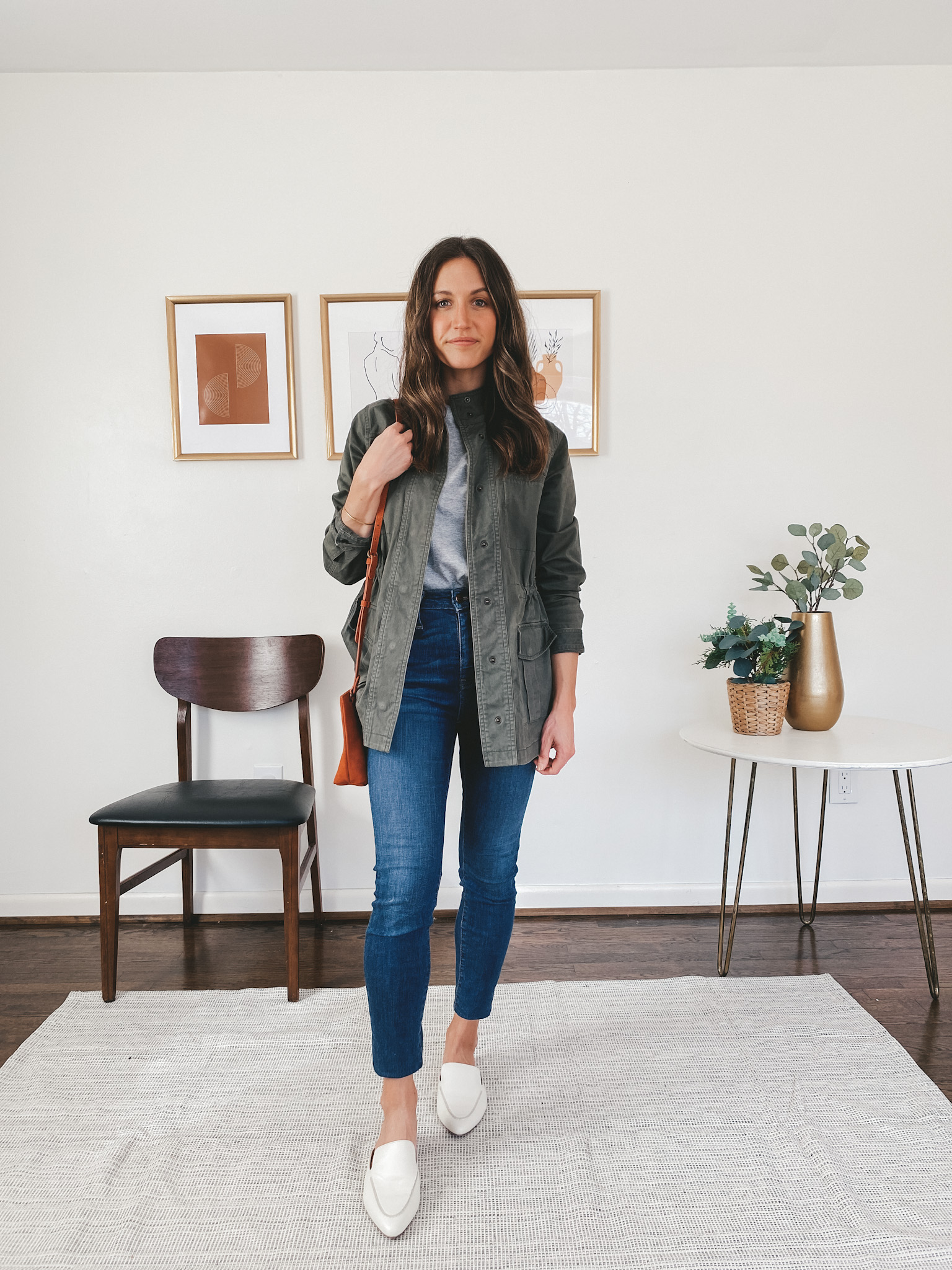 ashley wearing an Everlane gray tee, a Target green utility jacket, Madewell skinny jeans, Madewell white mules and a rust colored Target crossbody bag