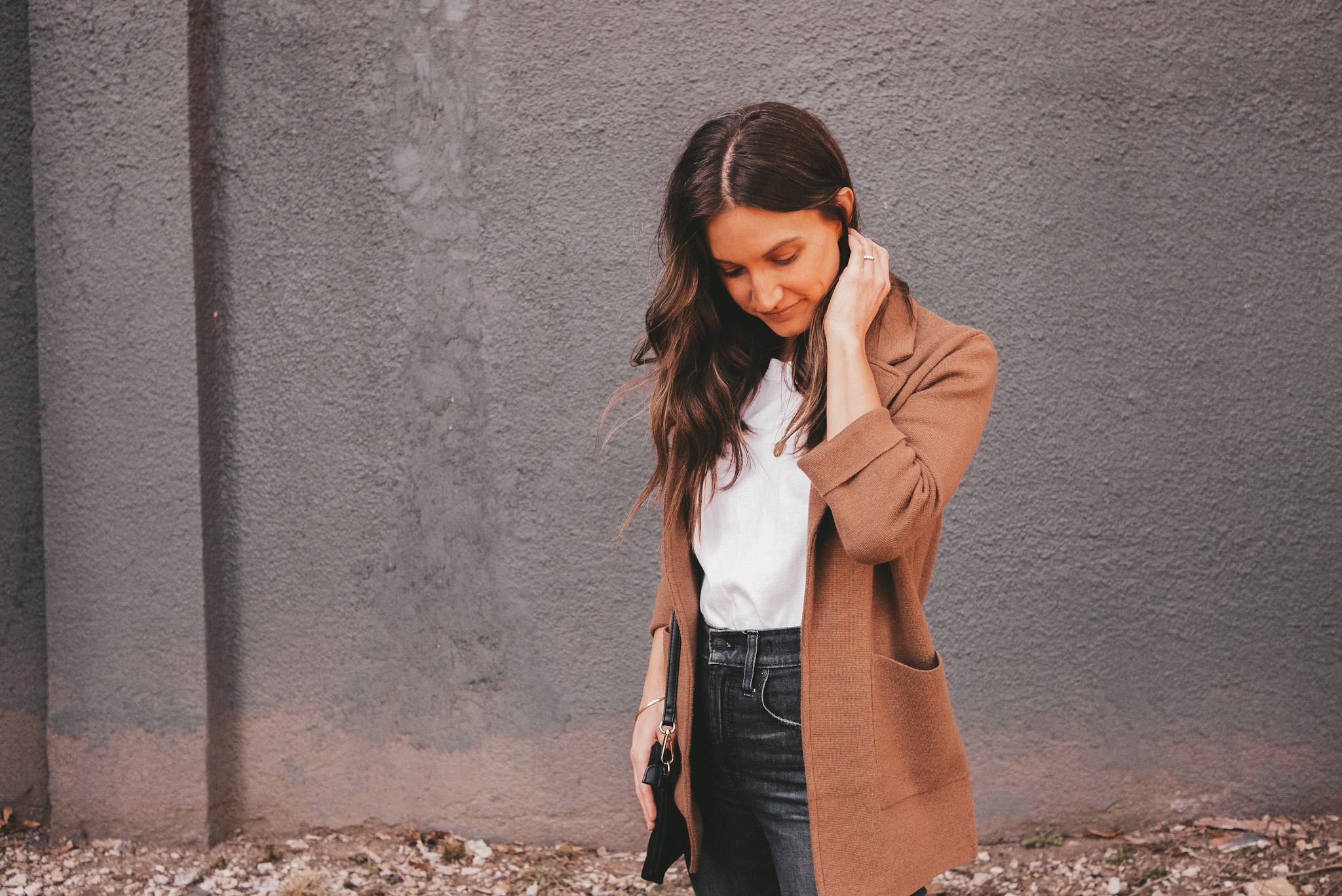 ashley wearing an Everlane white tee; a J.Crew sweater blazer, washed black Madewell perfect vintage jeans standing in front of a gray wall