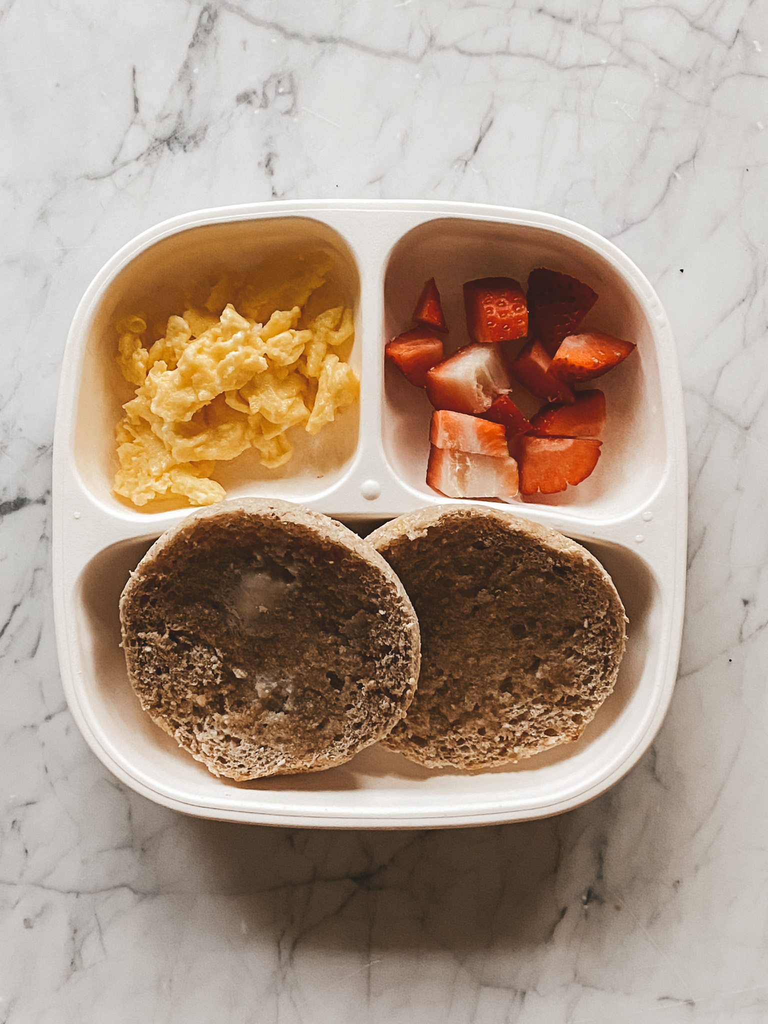 a toddler plate with an english muffin, strawberries and scrambled eggs