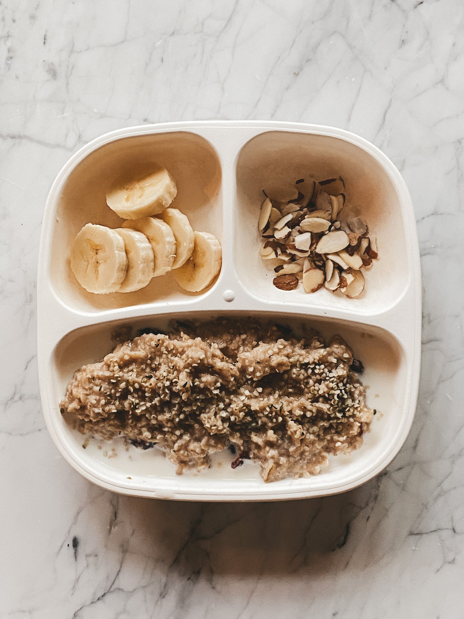 a white toddler plate with oatmeal, bananas, and sliced almonds