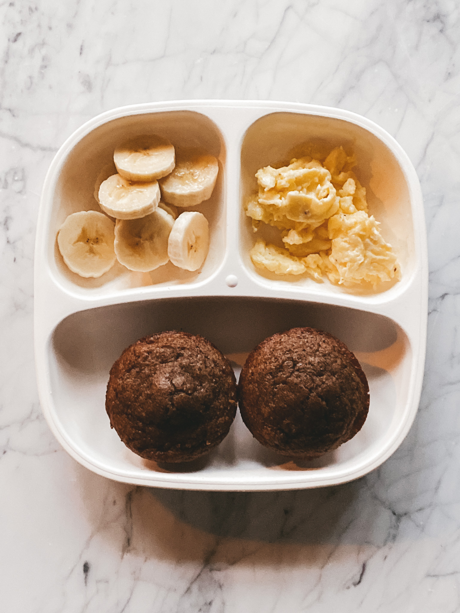 a white toddler plate with muffins, scrambled eggs and bananas