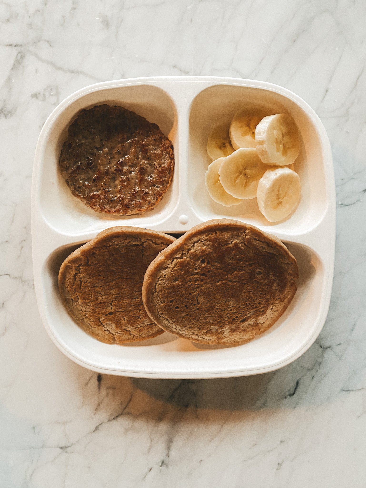 a white toddler plate with pancakes, bananas and sausage