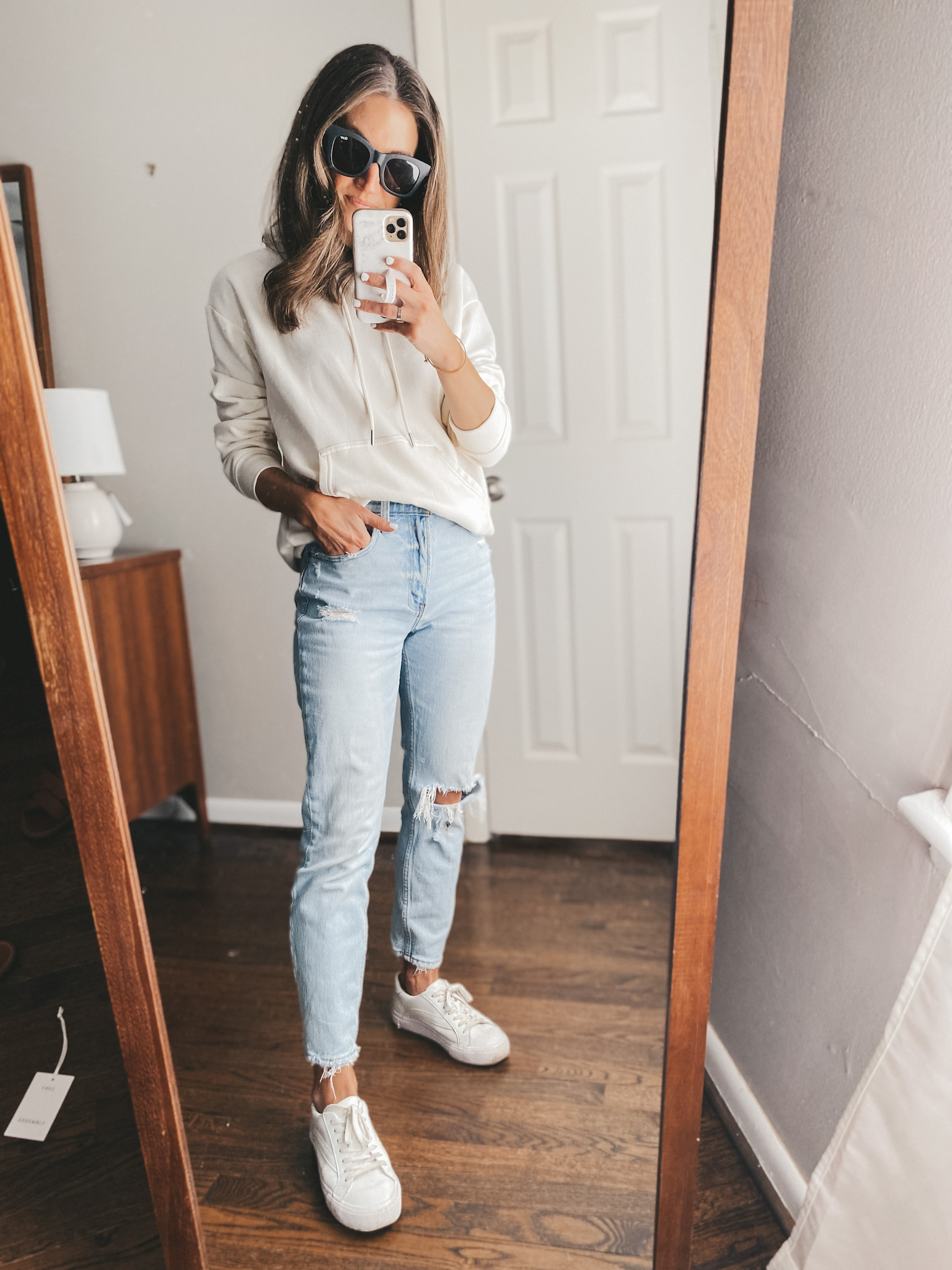ashley wearing a cream colored hoodie, distressed mom jeans and white sneakers