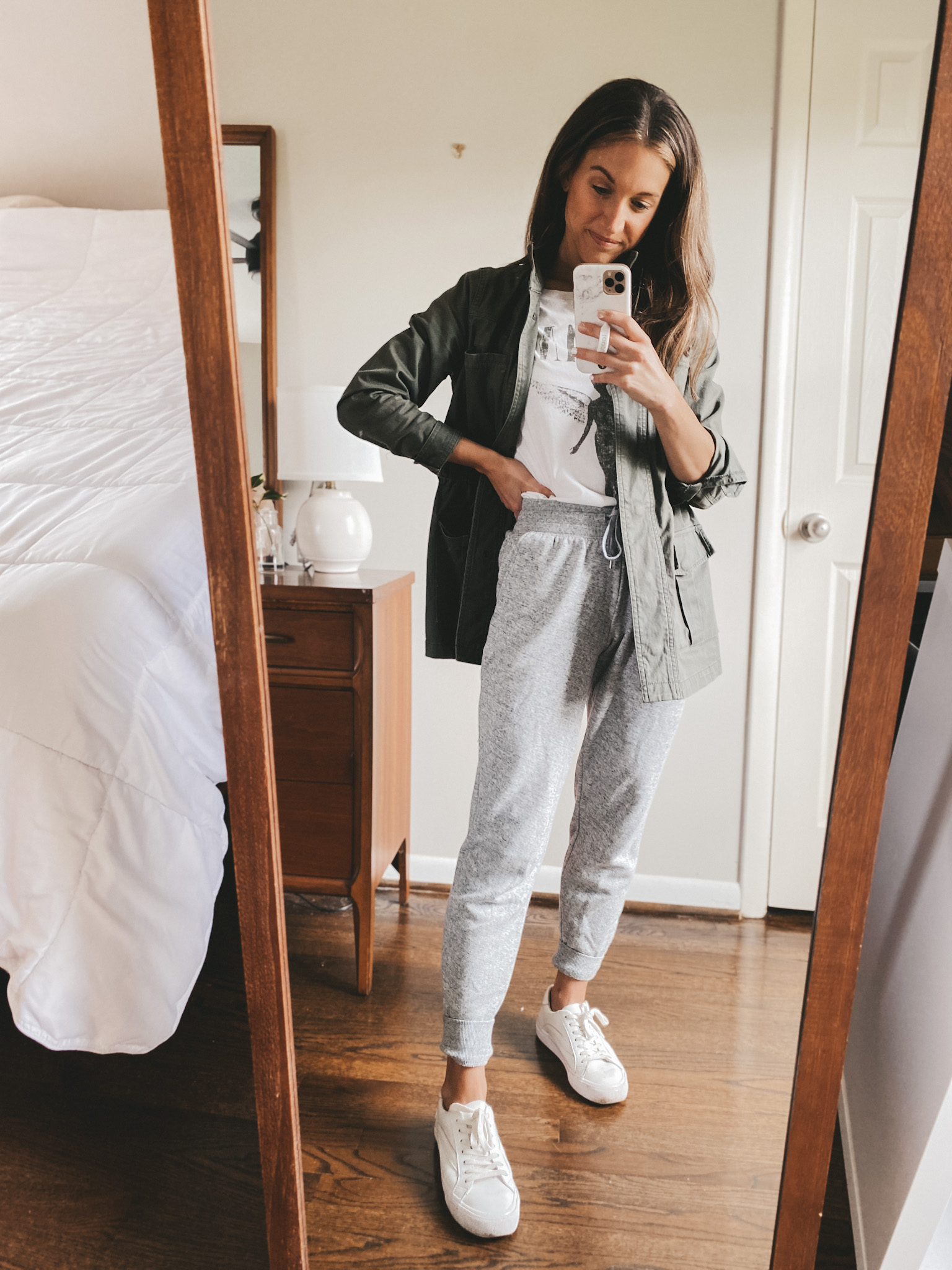 ashley wearing a white graphic tee, a green utility jacket, gray joggers, and white sneakers