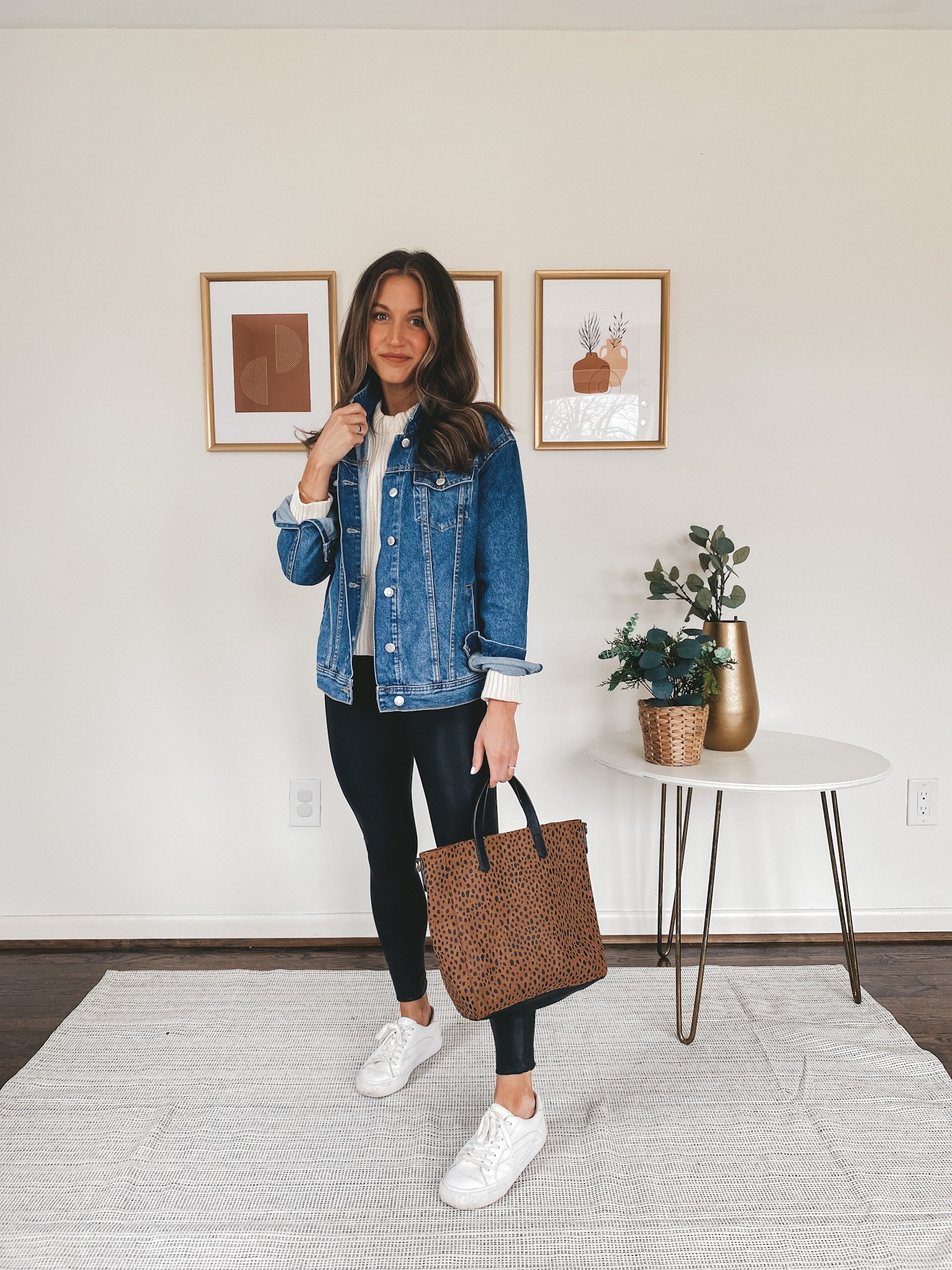 ashley wearing a cream sweater from Walmart, an Old Navy denim jacket, Spanx faux leather leggings, and Madewell white sneakers