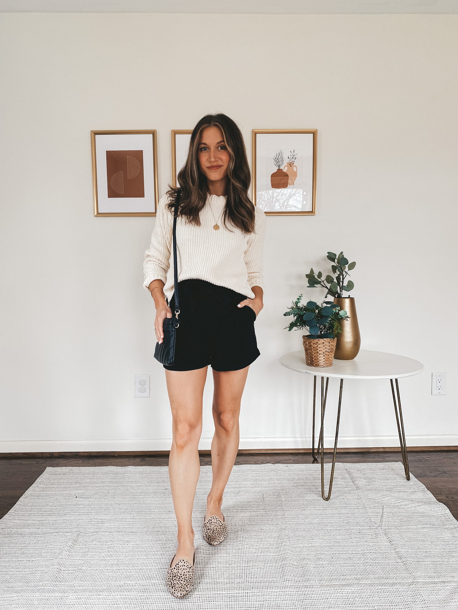 ashley wearing a cream sweater from Walmart, black paperbag shorts from H&M, leopard mules from Target, and a black quilted crossbody bag