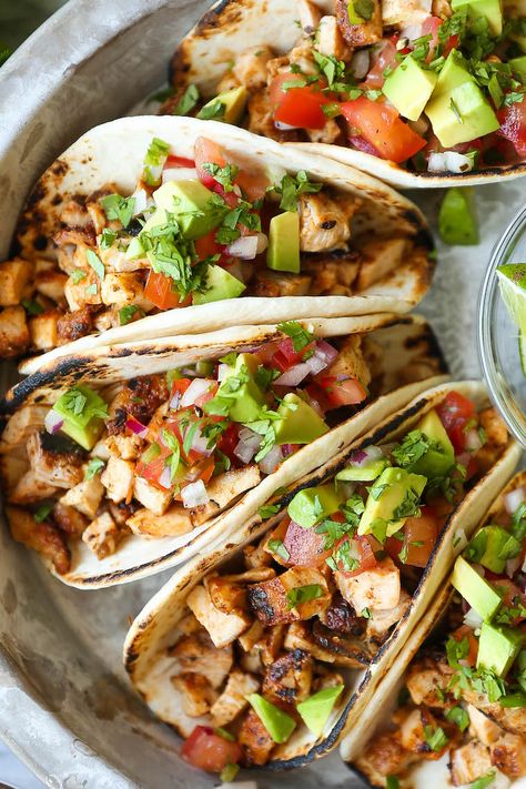 a serving platter of chicken tacos in flour tortillas topped with tomatoes and diced avocado