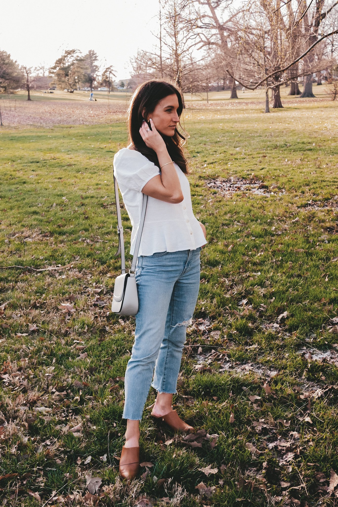 ashley wearing a white puff sleeve button front blouse, light wash jeans, and heeled mules in a park
