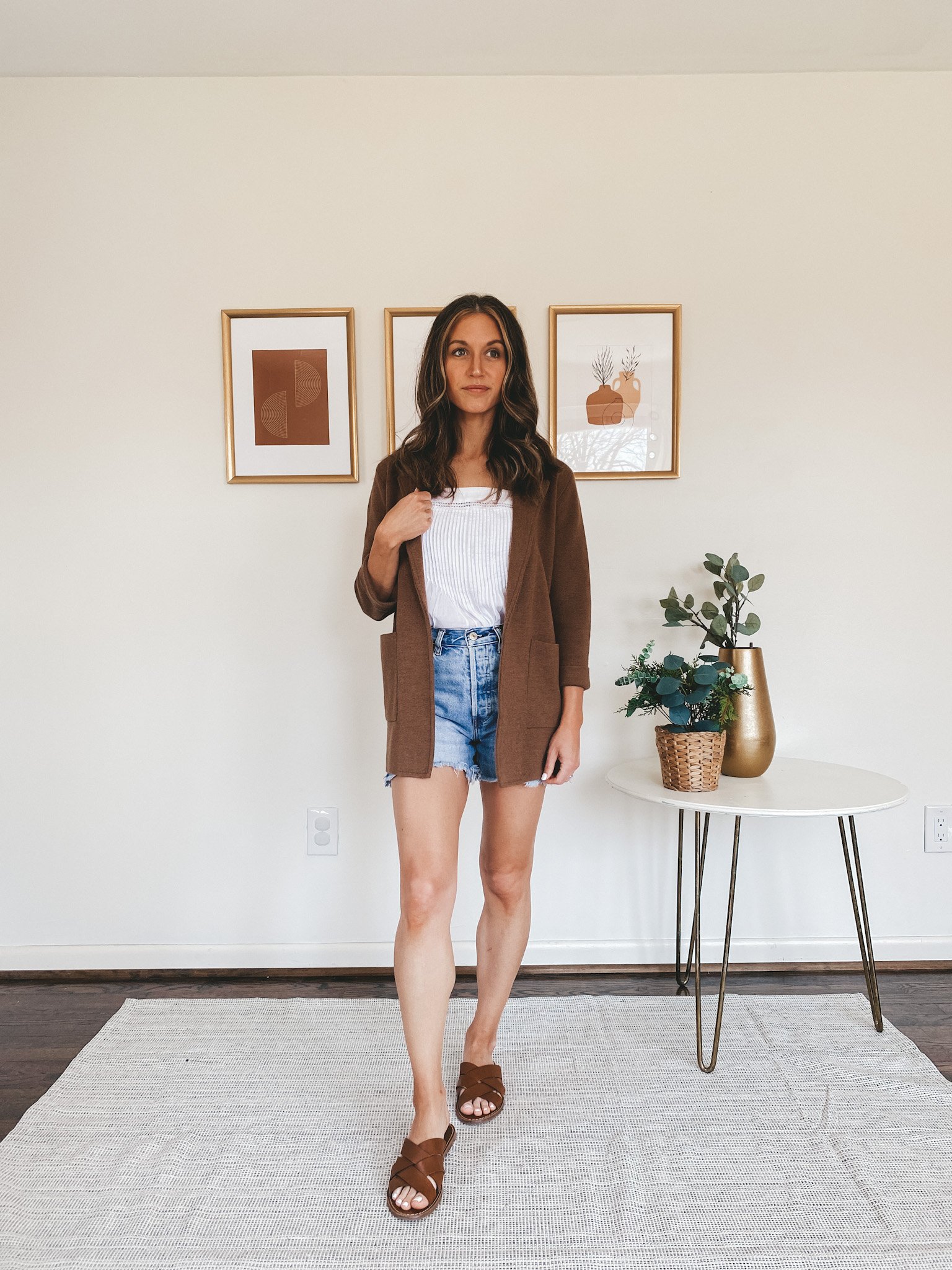 ashley wearing a white tank, brown sweater blazer, cut off denim shorts, and braided brown sandals