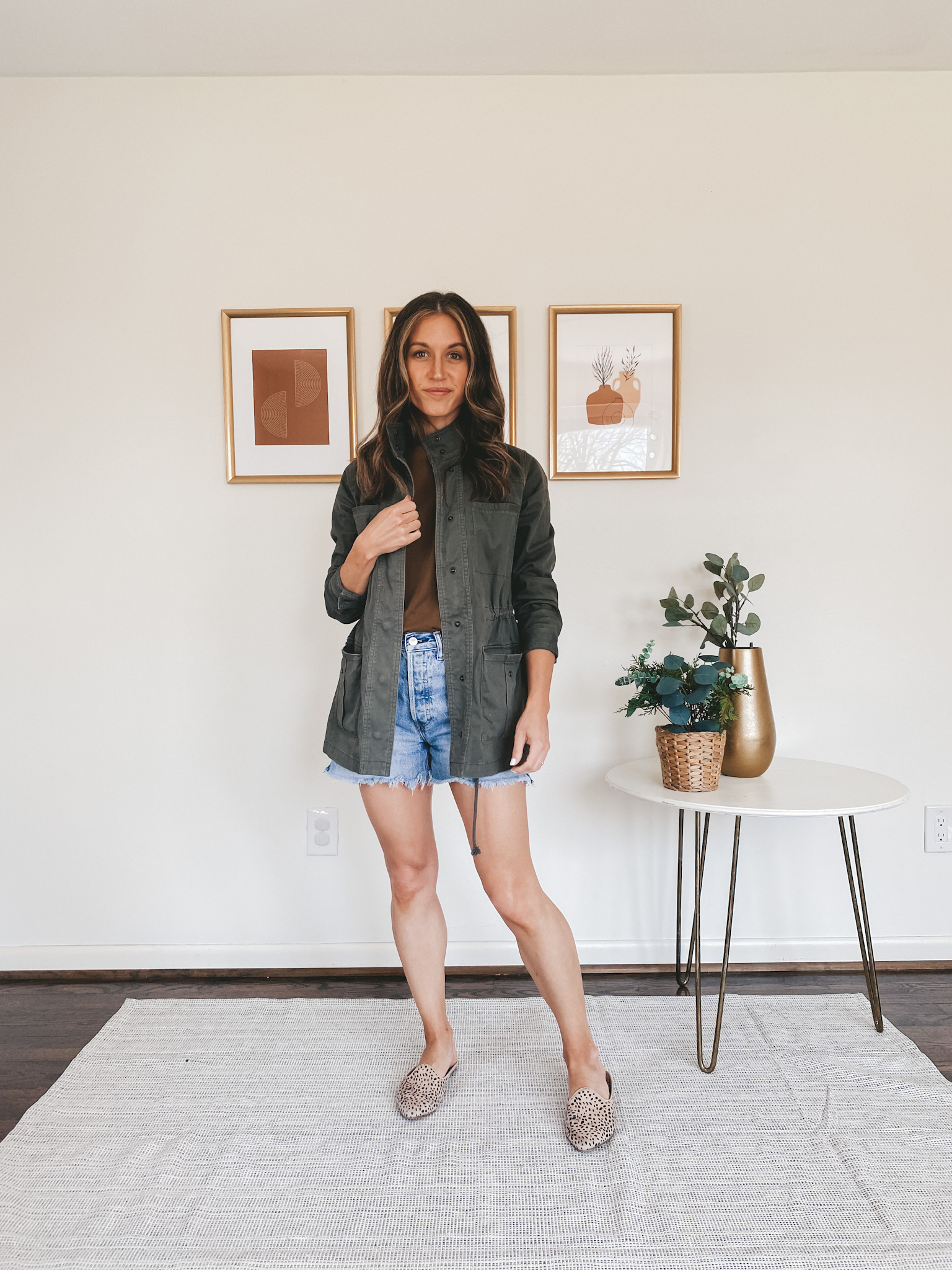 ashley wearing a green utility jacket, brown tee, cut off denim shorts and leopard mules