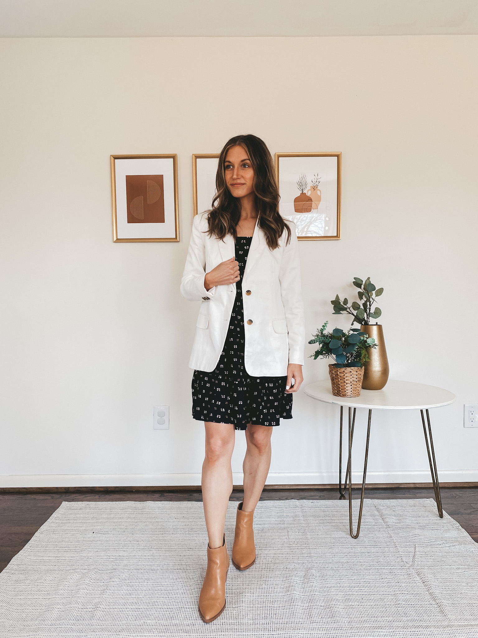 ashley wearing a black tiered mini dress, white blazer, and camel colored ankle boots