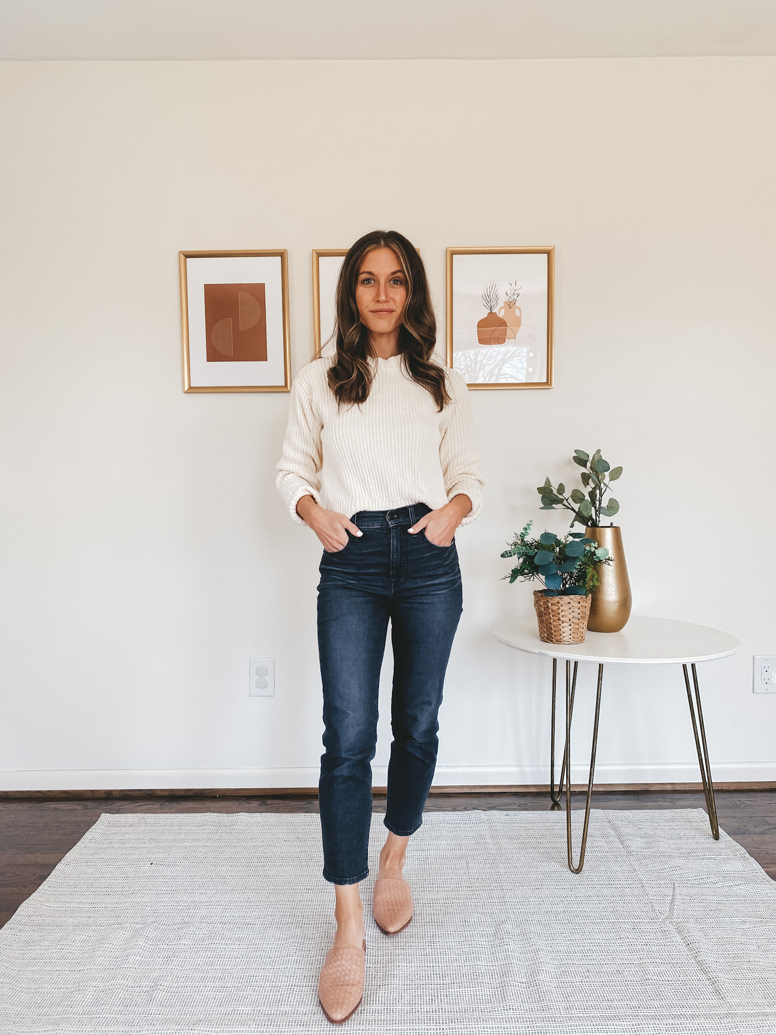 ashley wearing a cream sweater, black denim and woven mules