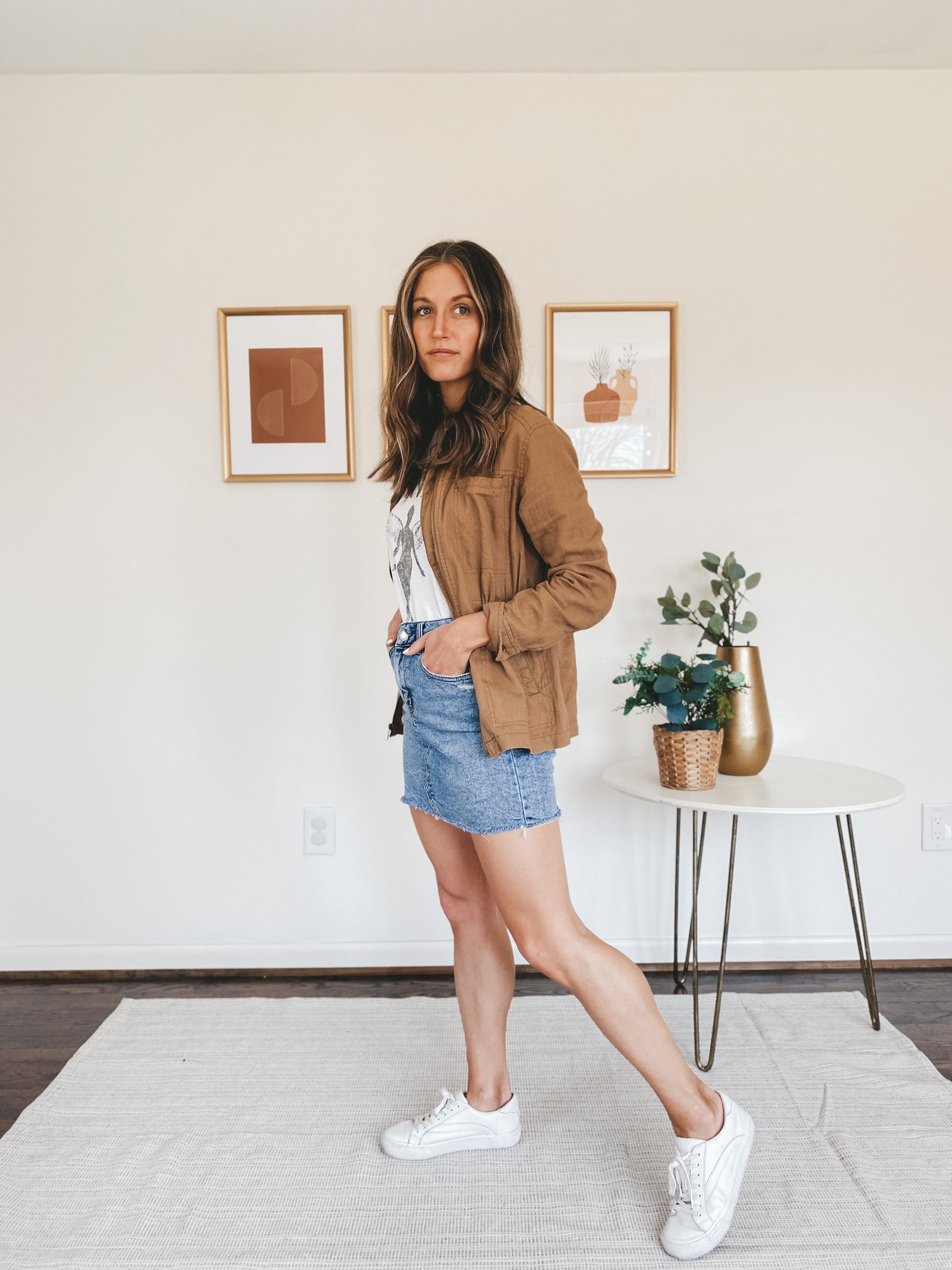 ashley wearing a white graphic tee, tan utility jacket, denim skirt and white sneakers