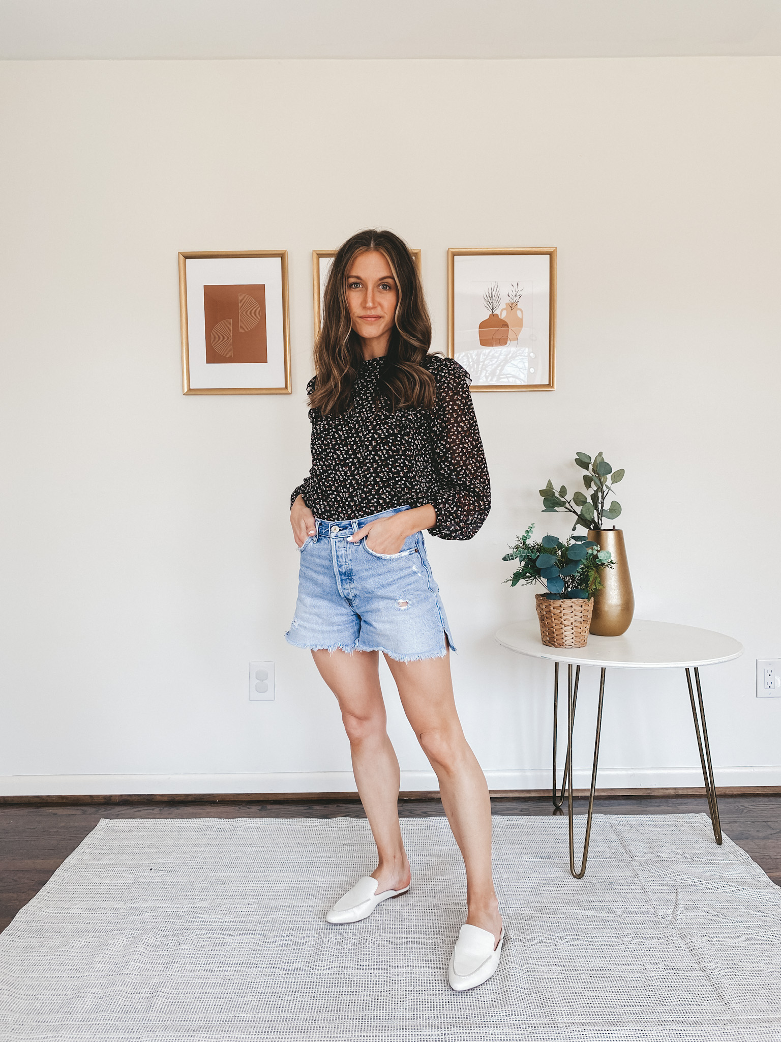 ashley wearing a black floral top, cut off denim shorts, and white mules