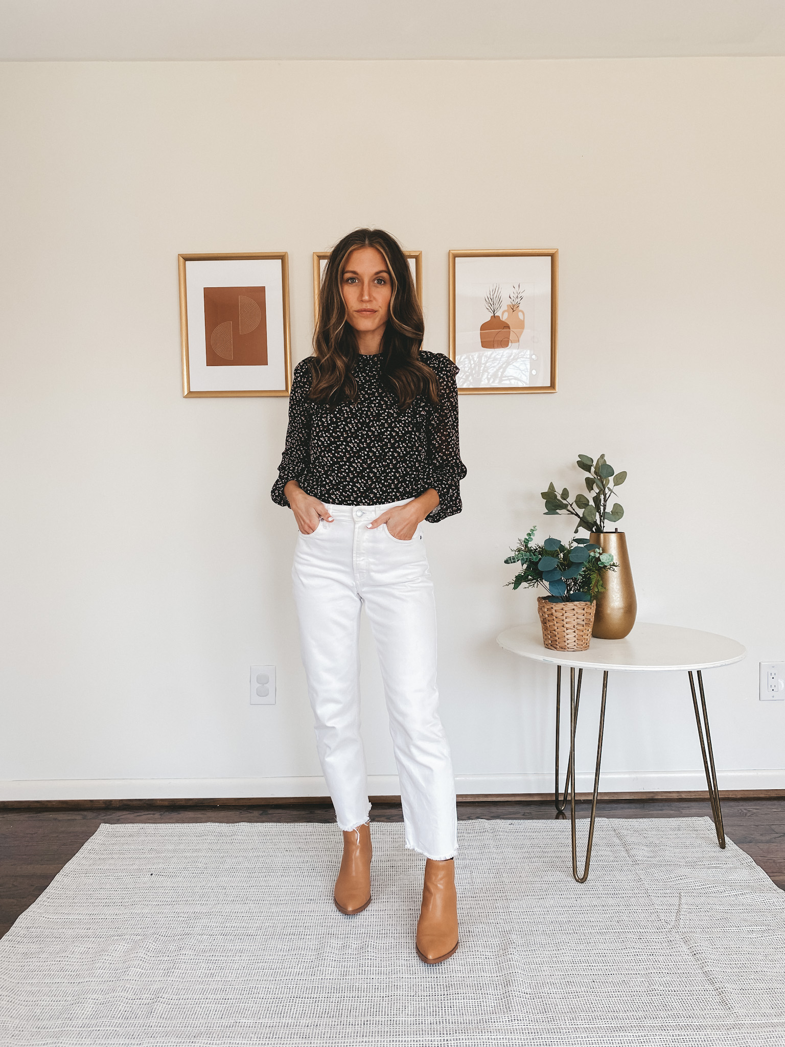 ashley wearing a black floral top, white jeans, and camel ankle booties