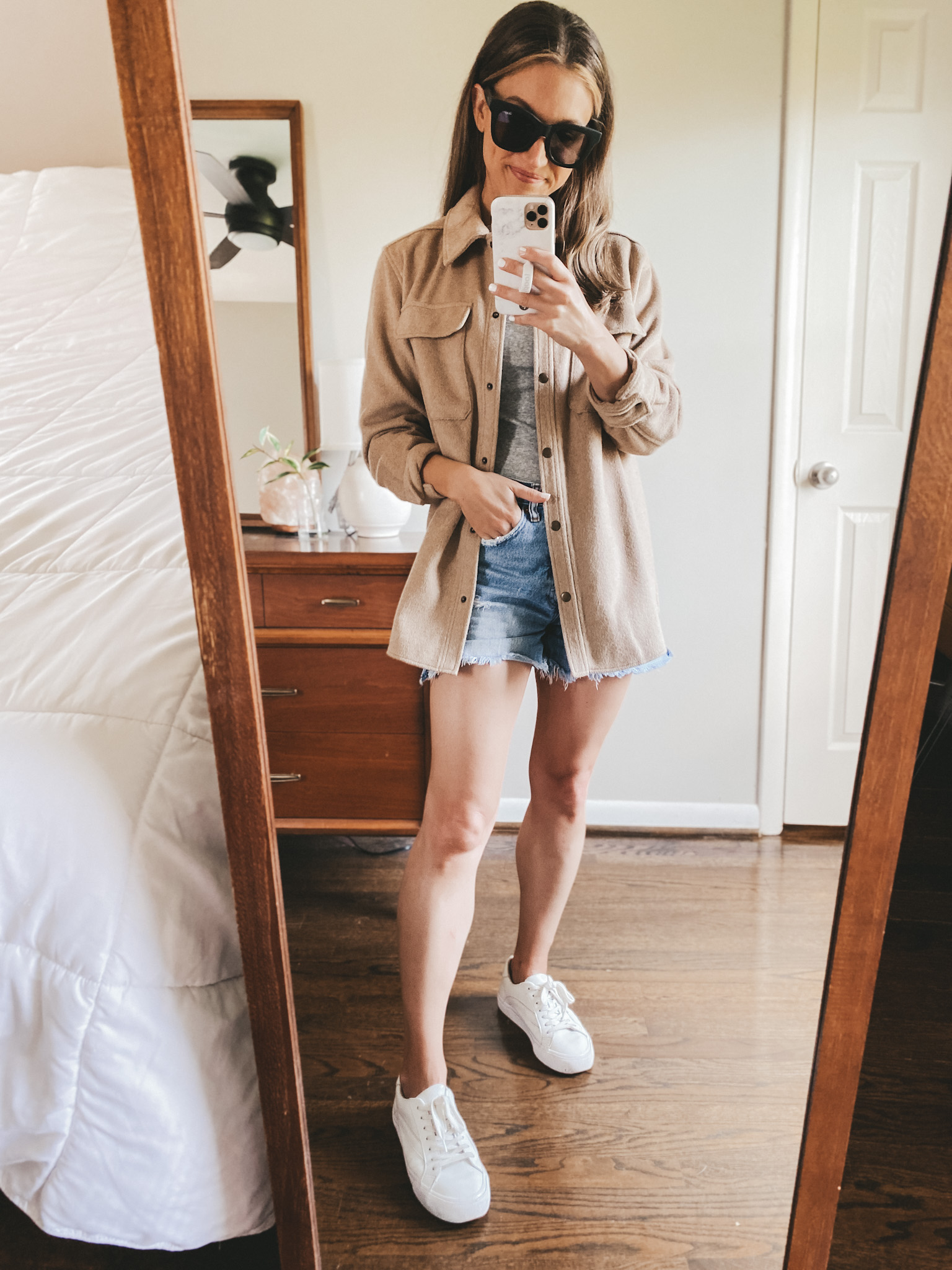 ashley wearing a gray tee, tan colored shacket, cut-off denim shorts and white sneakers