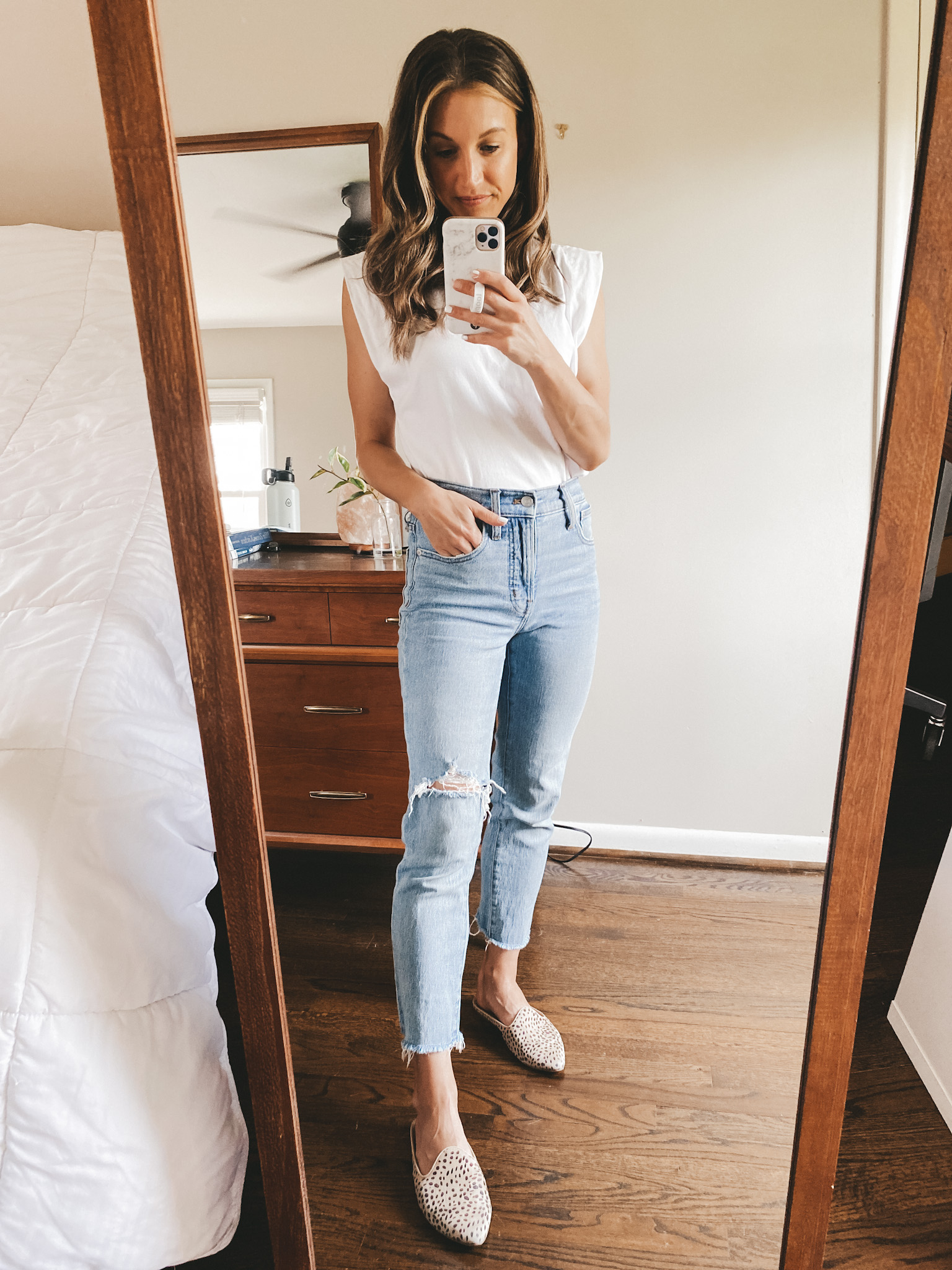 ashley wearing a white muscle tee, straight leg light wash distressed jeans, and leopard mules