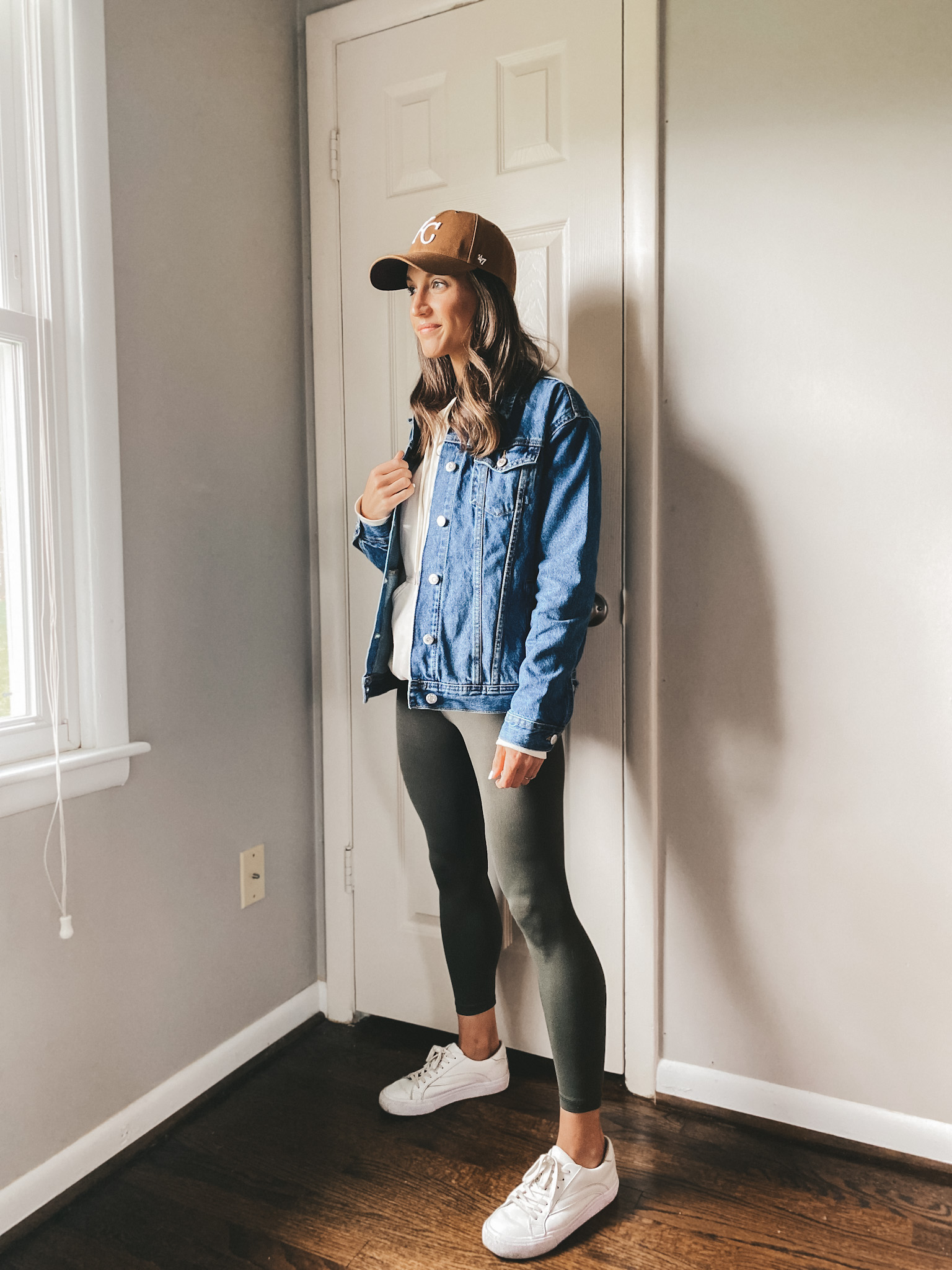 ashley wearing a cream colored hoodie, denim jacket, olive leggings, and white sneakers