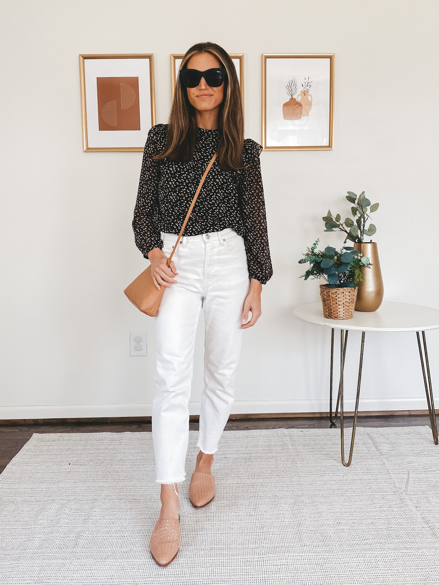 ashley wearing a black long sleeved floral blouse, white denim, and tan woven mules