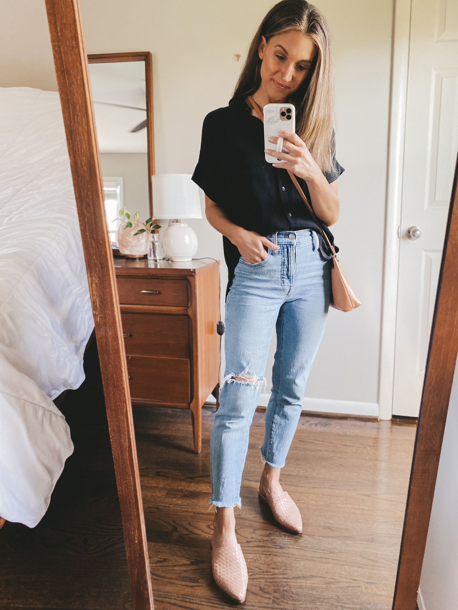ashley wearing a black drapey button down from Madewell, distressed light wash jeans, and tan woven mules
