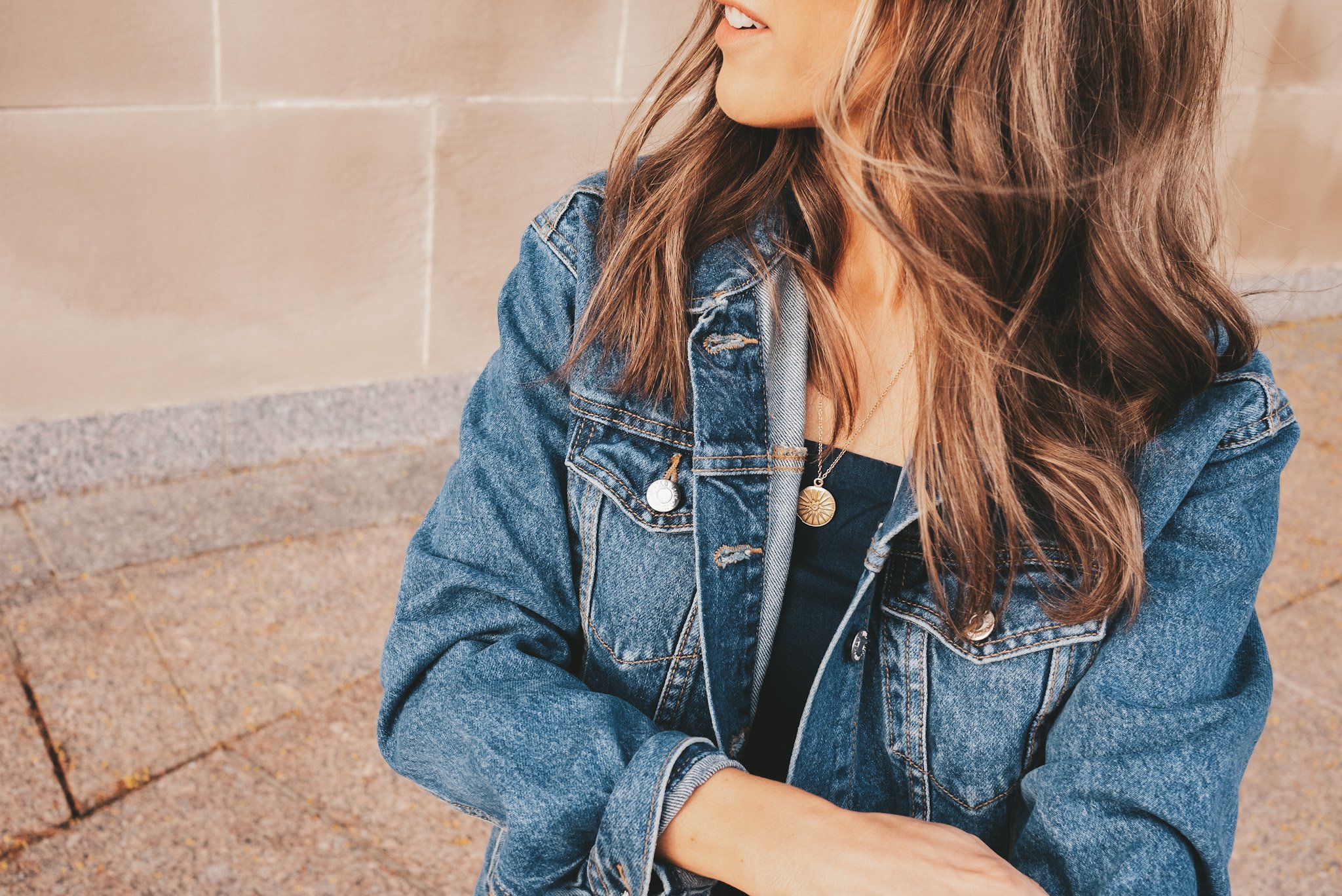 ashley wearing a chambray romper, oversized denim jacket, white sneakers, and square frame black sunglasses walking down stairs at The Nelson Atkins Museum in Kansas City
