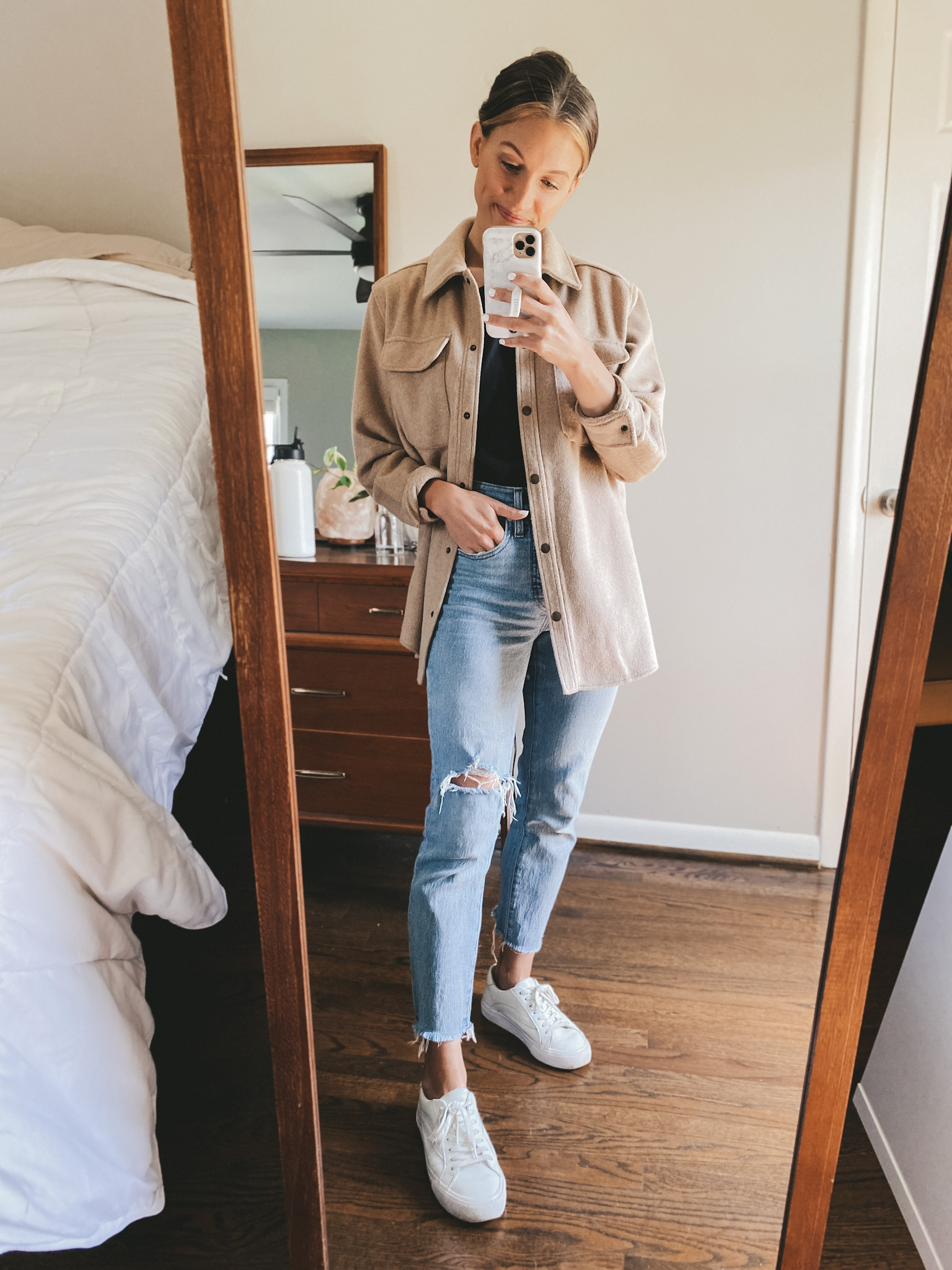 ashley wearing a black tee, tan shacket, light wash distressed denim and white sneakers