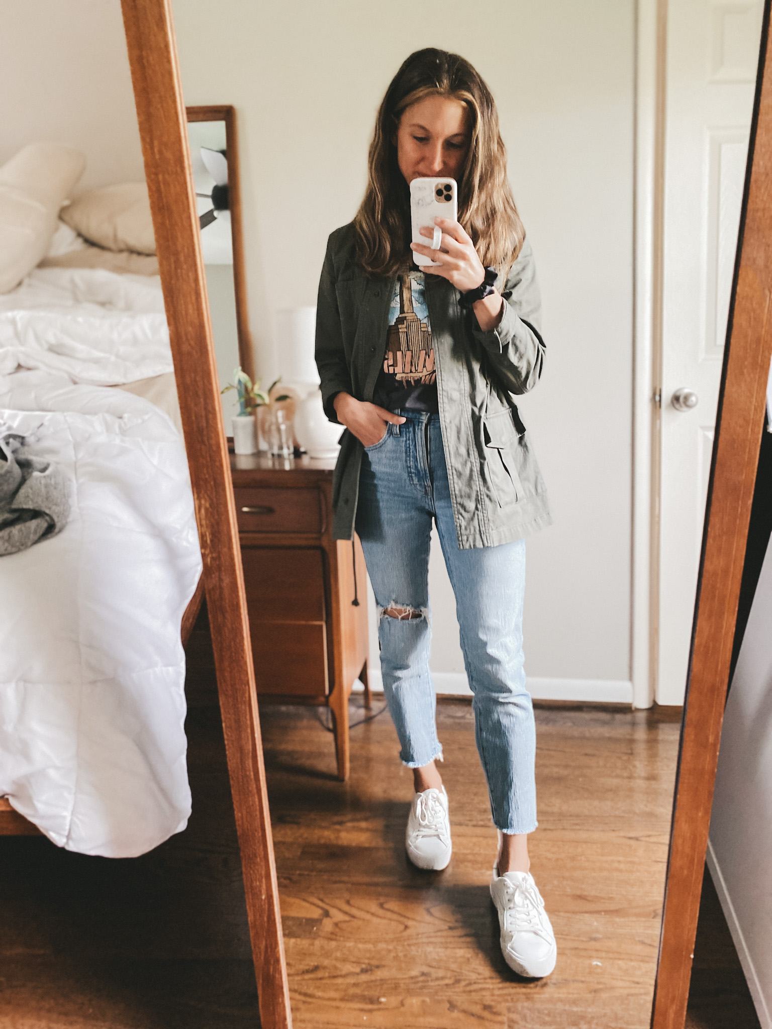 ashley wearing a black graphic tee, green utility jacket, and light wash distressed jeans and white sneakers