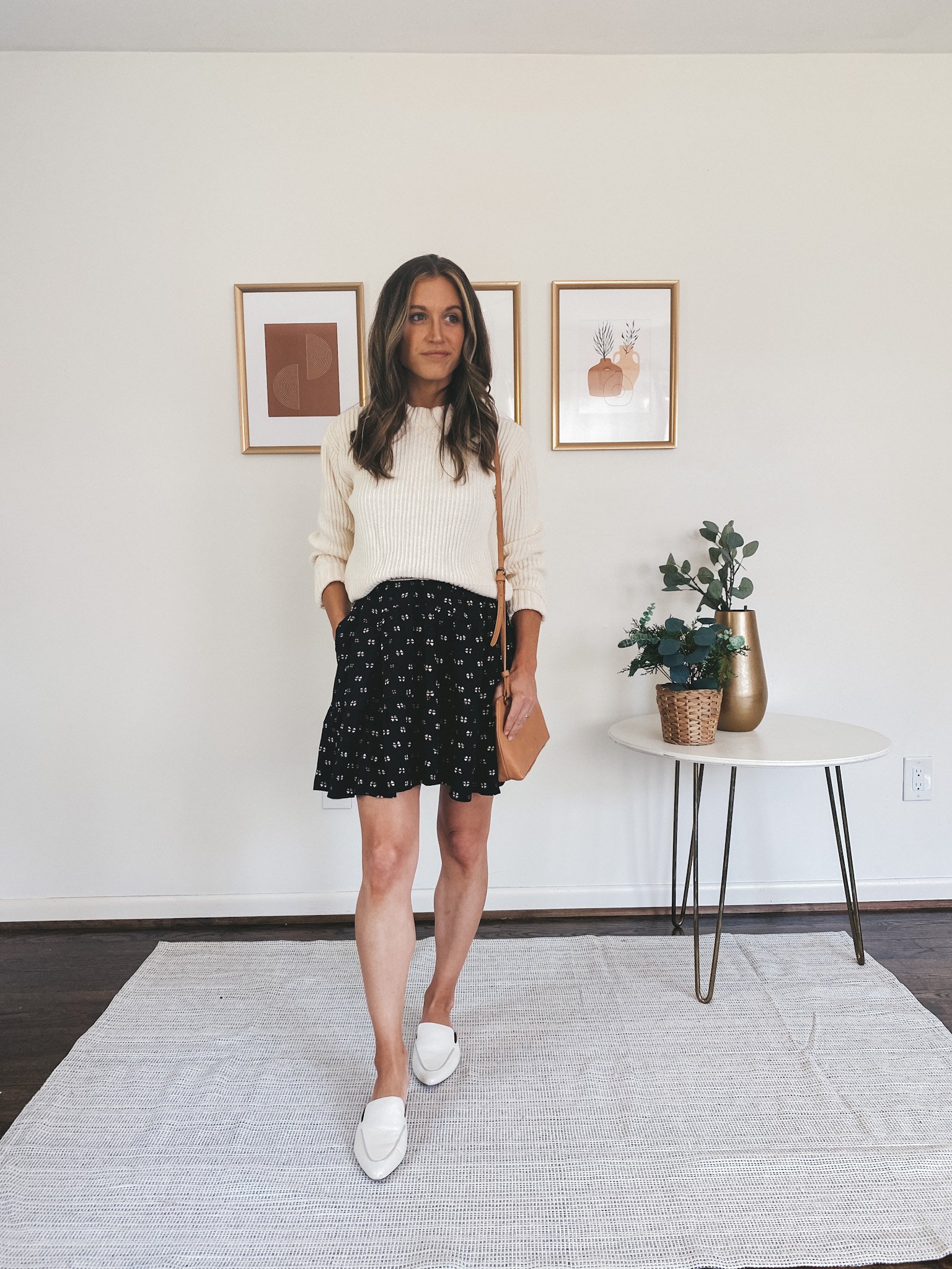 ashley wearing a cream sweater over a black mini dress and white mules