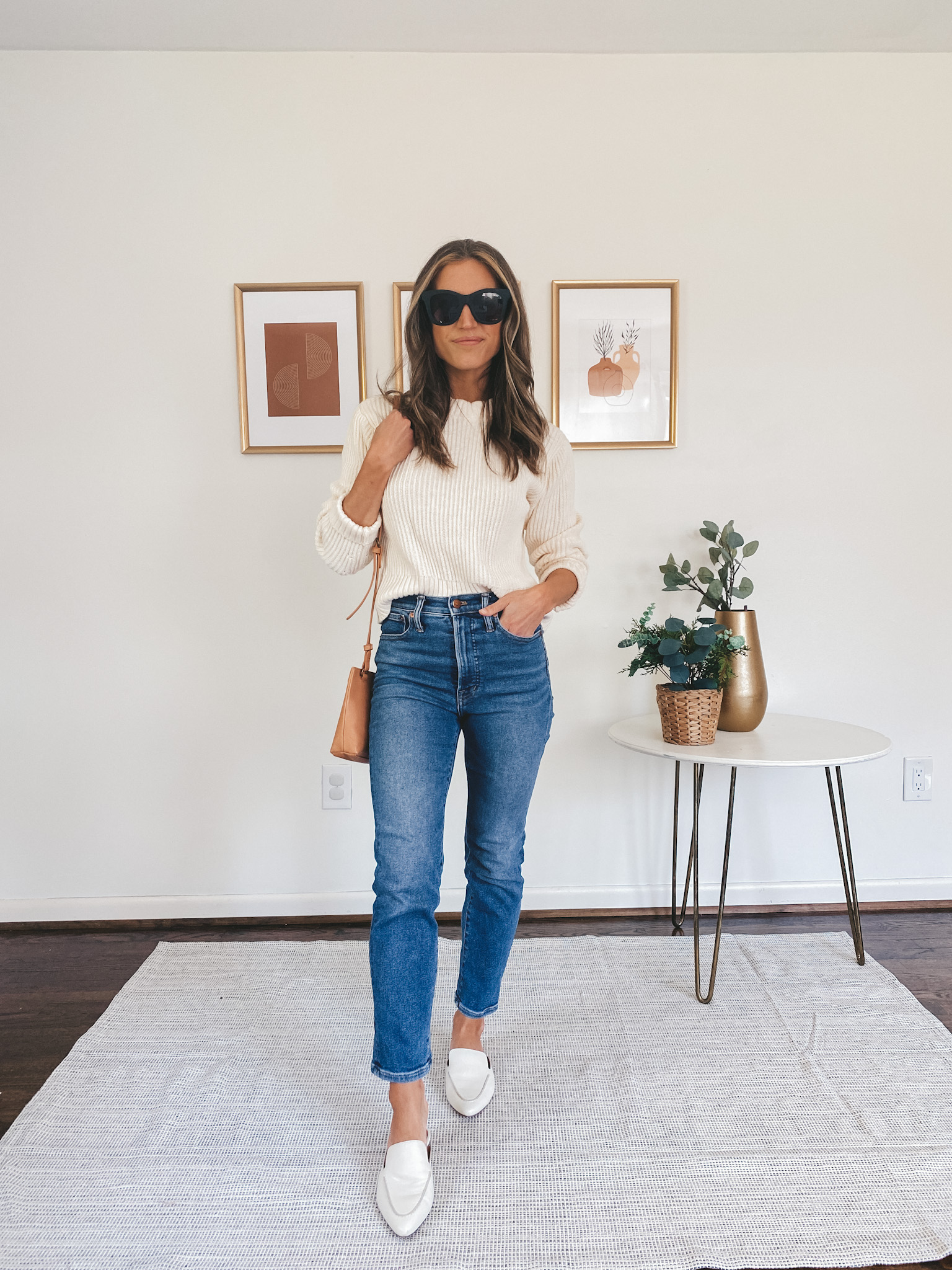 ashley wearing a cream sweater, mid-wash straight leg denim, white mules and square frame black sunglasses