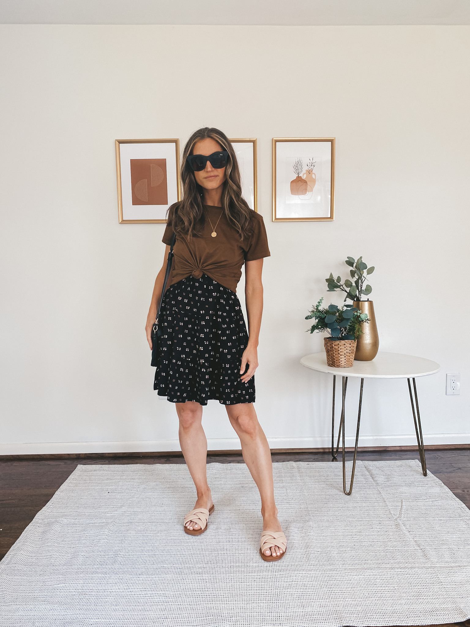 ashley wearing a brown tee over a black patterned dress, and nude padded slides