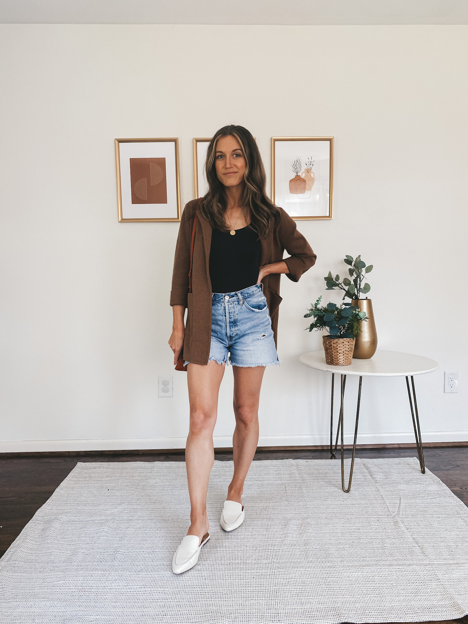 ashley wearing a black bodysuit, brown sweater blazer, denim cut off shorts and white mules